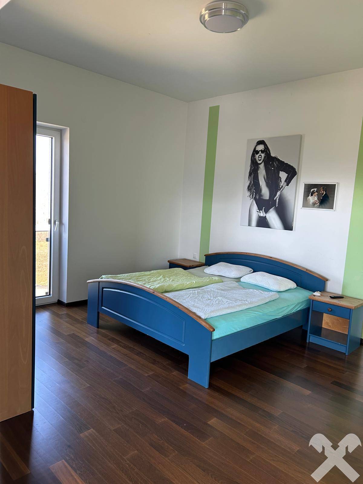Schlafzimmer mit Holzboden, blauem Bett und Zugang zu einem Balkon oder einer Terrasse.