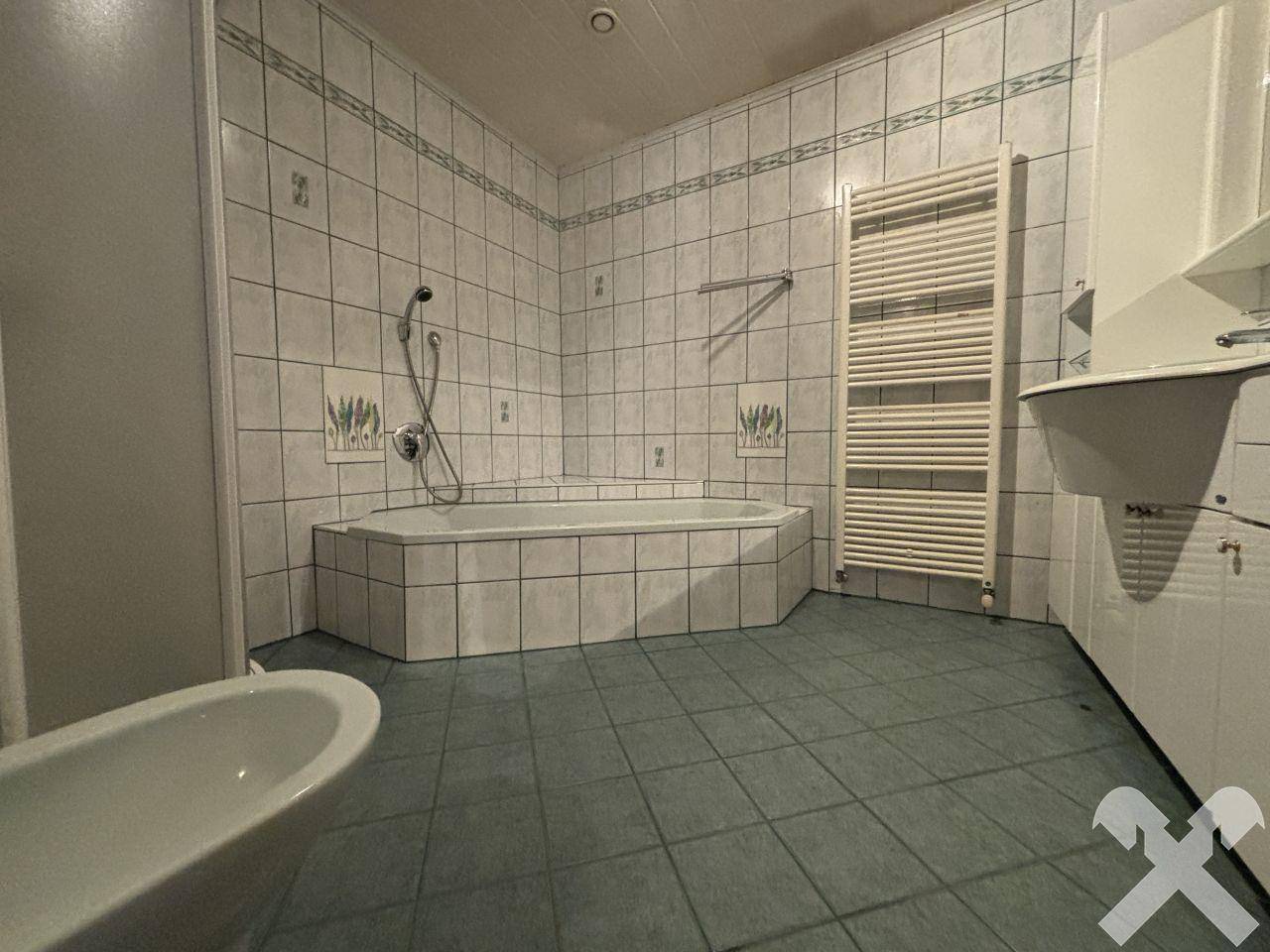 Badezimmer mit Eckbadewanne, Fliesenboden und beheiztem Handtuchhalter.
