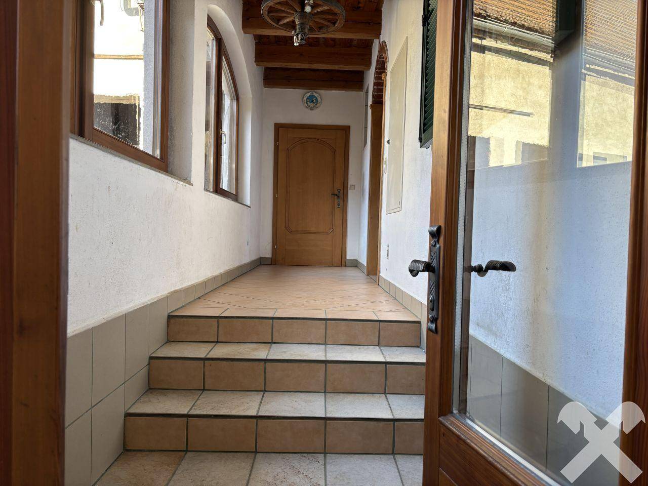 Heller Eingangsbereich mit gefliestem Boden, Holztreppe und rustikalen Holztüren.