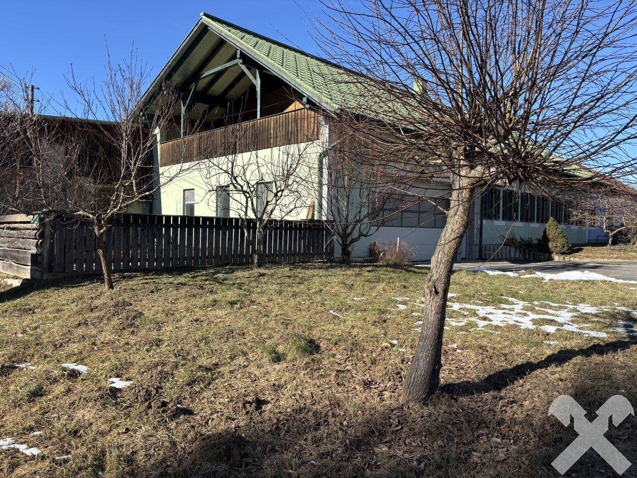 Seitenansicht des Hauses mit Holzbalkon, Zaun und kahlen Bäumen im Vorgarten.