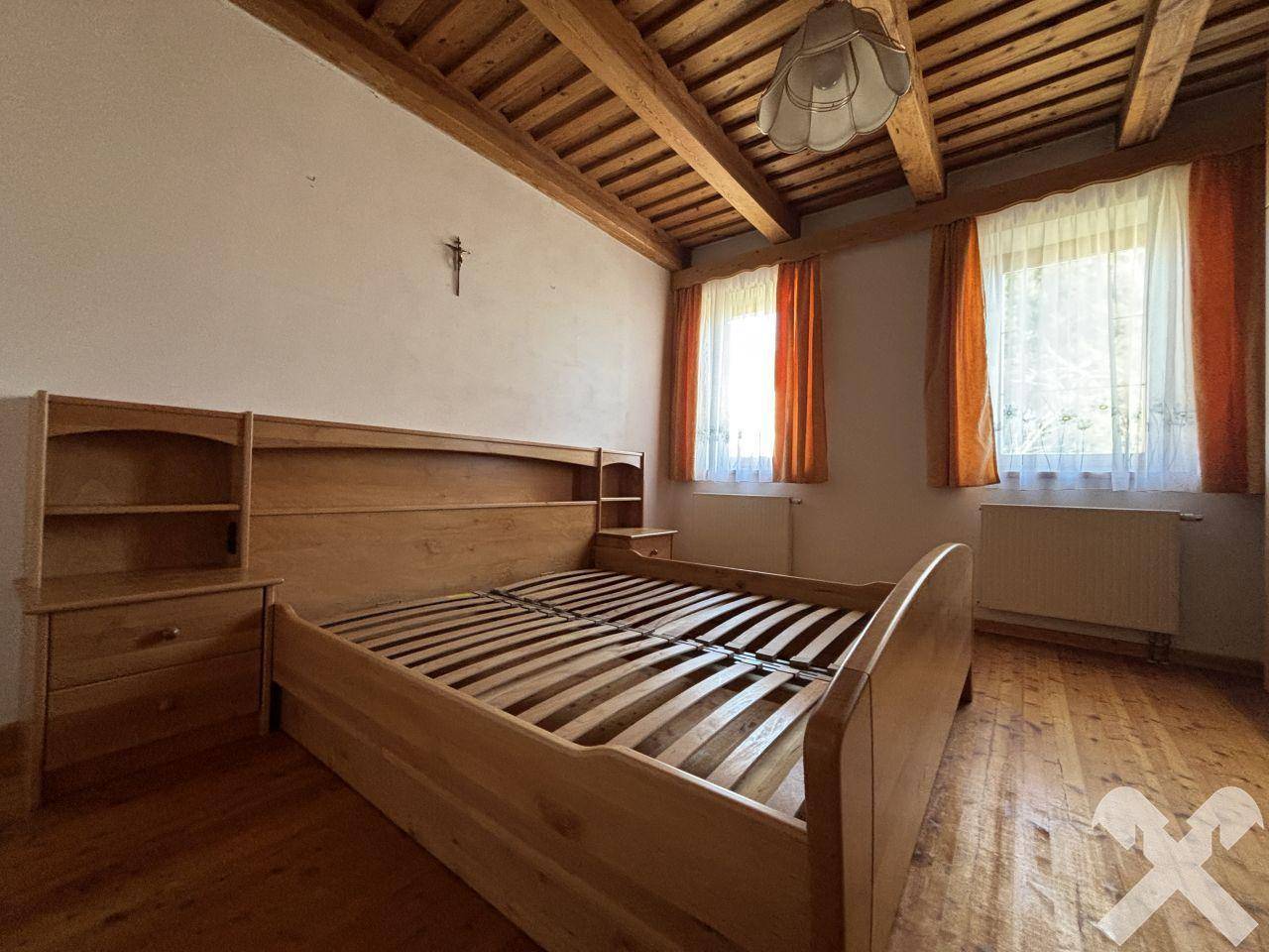 Schlafzimmer mit Holzbett, Holzbalkendecke und Blick ins Grüne durch die Fenster.