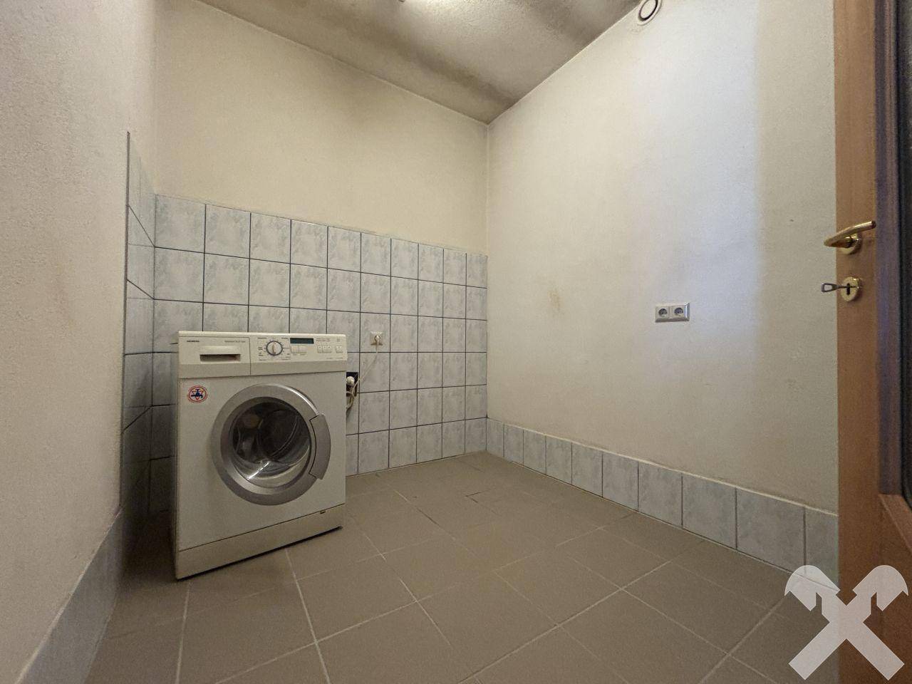 Hauswirtschaftsraum mit Waschmaschine, gefliestem Boden und teilweise gefliesten Wänden.