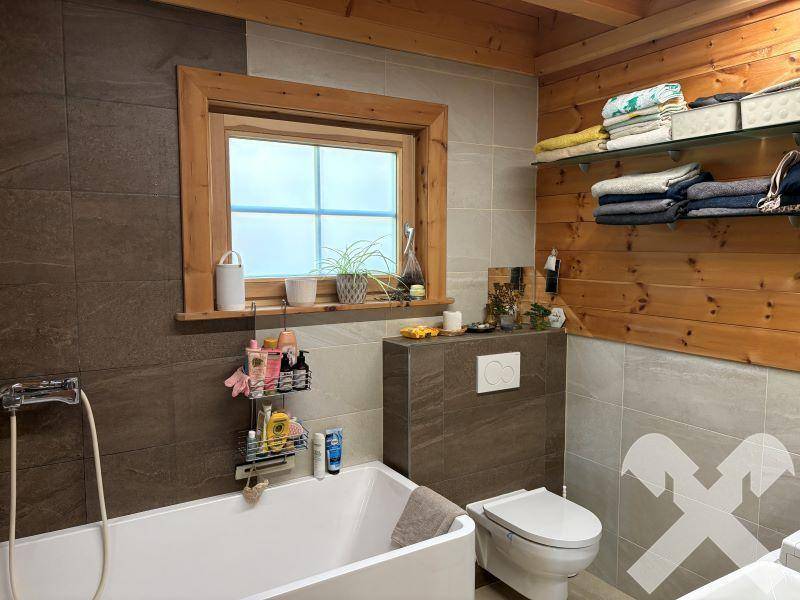 Modernes Badezimmer mit Badewanne, Wand-WC und Fliesen in Grau- und Brauntönen.