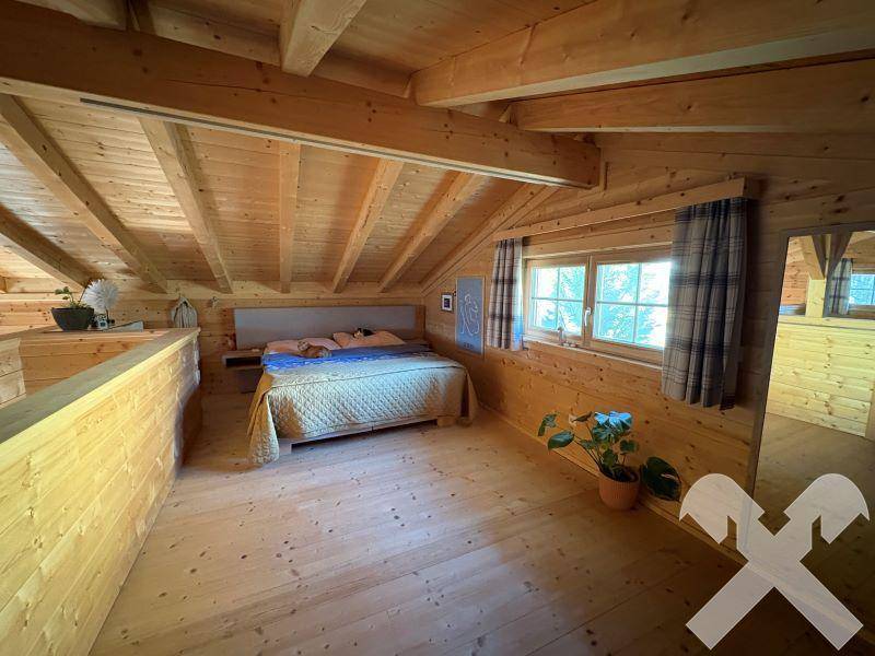 Geräumiges Schlafzimmer im Dachgeschoss mit sichtbaren Holzbalken und viel Tageslicht.