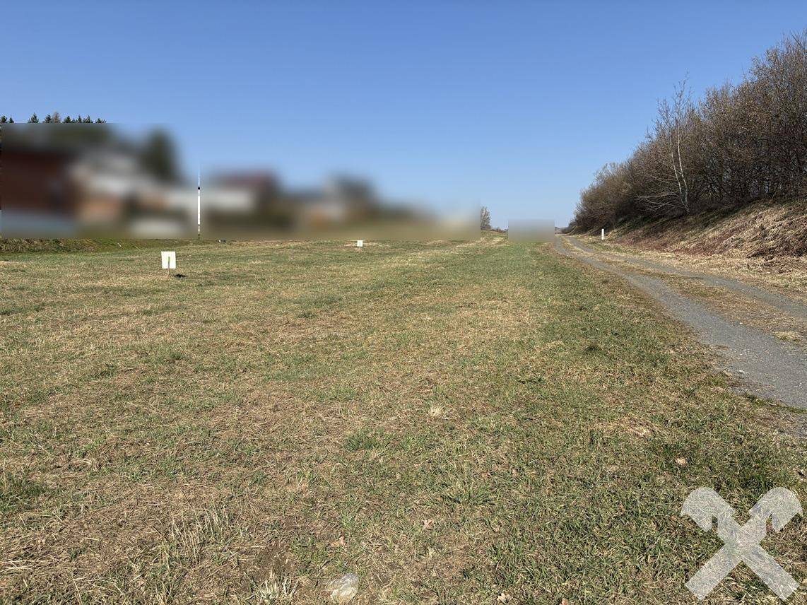 Weitläufiges Grundstück mit Grasfläche und unbefestigtem Weg unter blauem Himmel.
