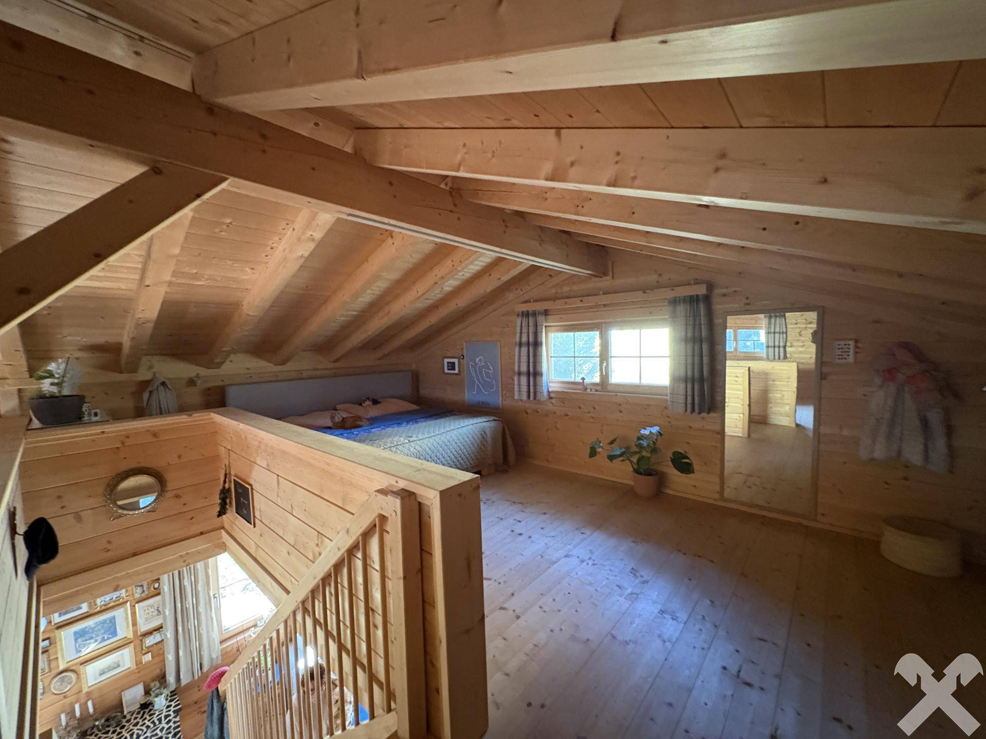 Offenes Schlafzimmer im Dachgeschoss mit Holzbalken und viel natürlichem Licht.