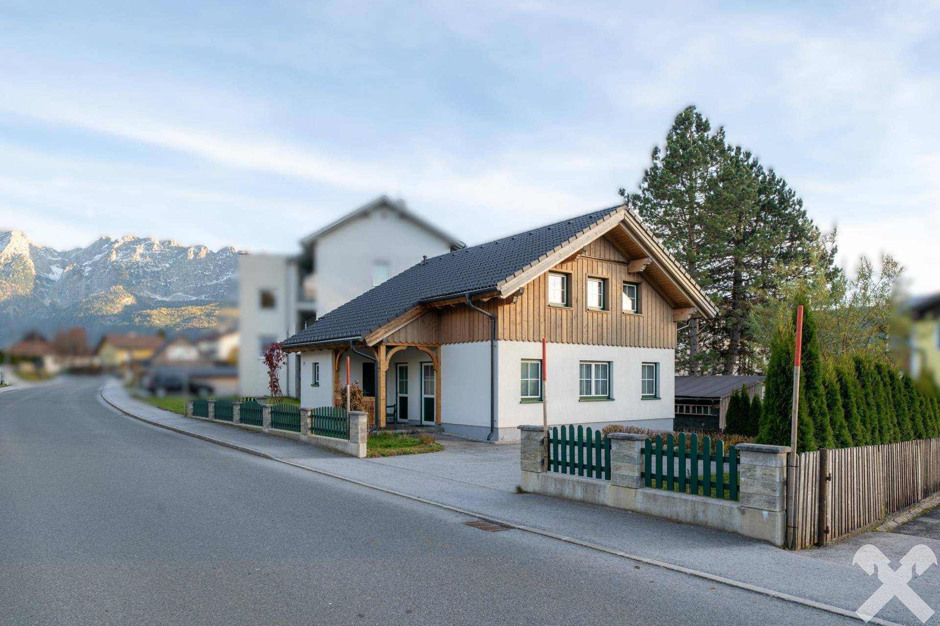 Modernes Einfamilienhaus mit Holzfassade und Satteldach, umgeben von einem gepflegten Vorgarten und mit beeindruckendem Bergblick.