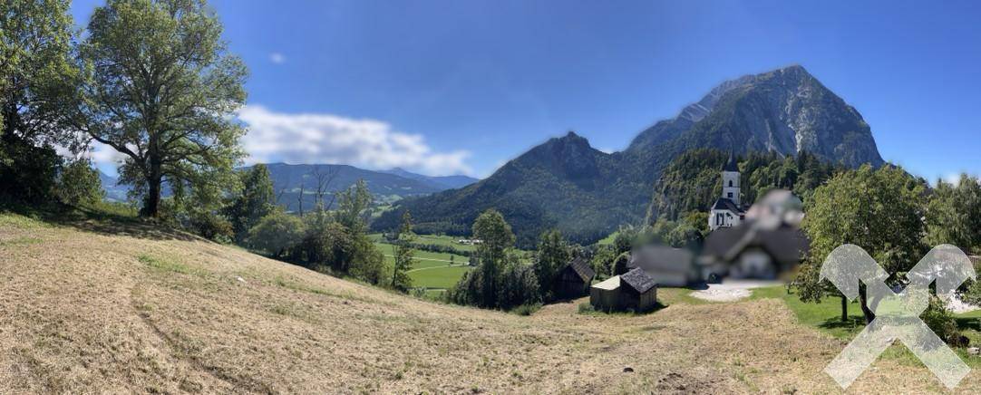 Panoramablick über sanfte Hügel, ein charmantes Dorf mit Kirche und majestätische Berge am Horizont.