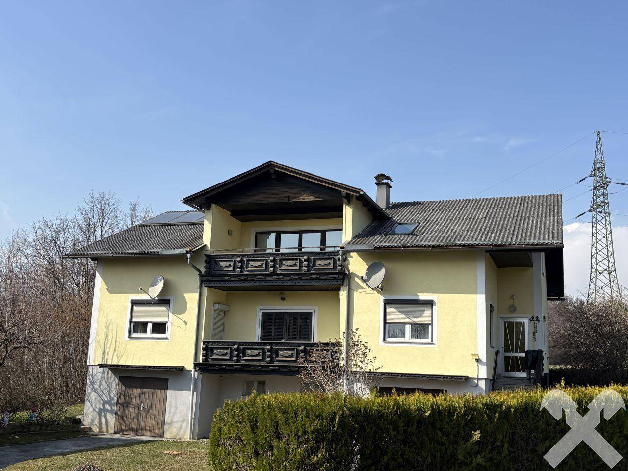 Ansicht des gelben Einfamilienhauses mit Balkonen und einer grünen Hecke im Vorgarten.