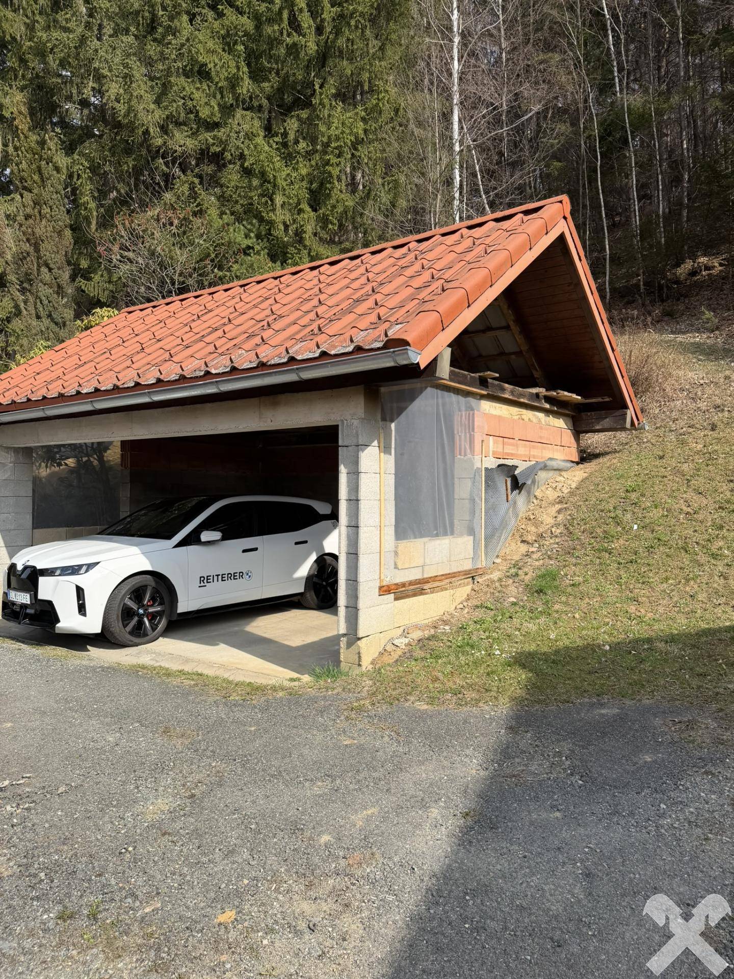 Überdachter Carport mit einem geparkten Auto, eingebettet in die natürliche Hanglage.