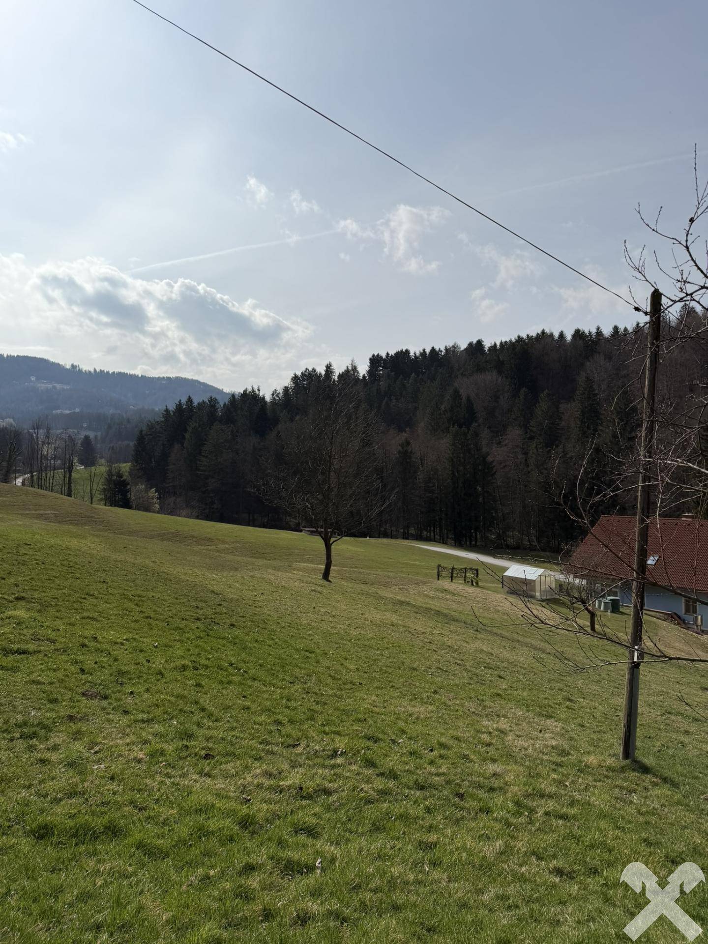 Weitläufige grüne Wiesen und bewaldete Hügel unter blauem Himmel, mit dem Haus in der Ferne.