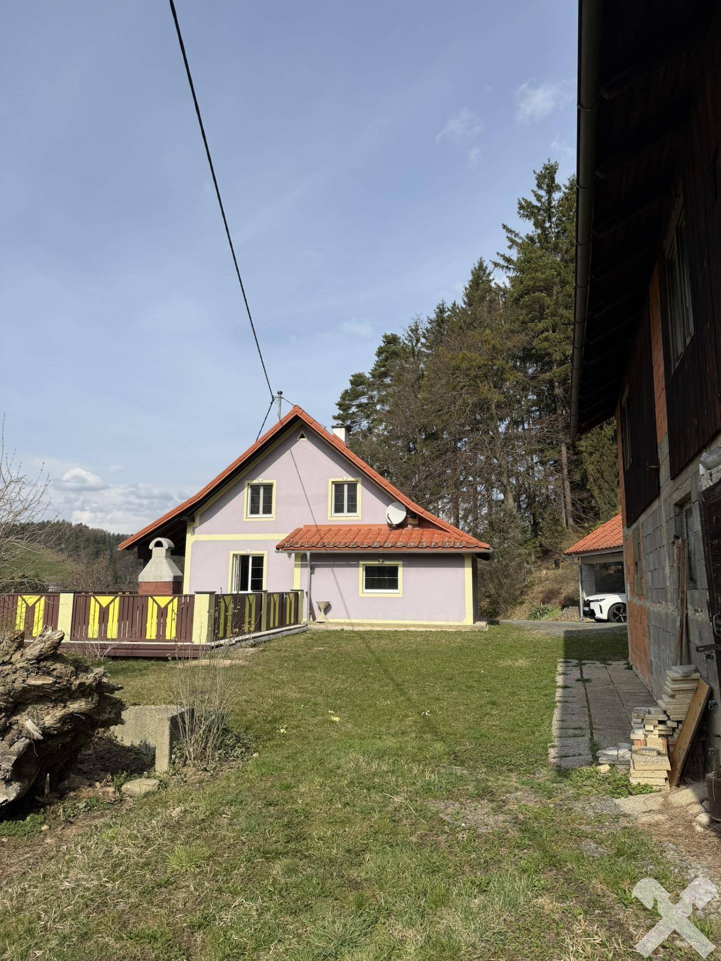 Hausansicht mit angrenzendem Nebengebäude und Blick auf den Wald im Hintergrund.