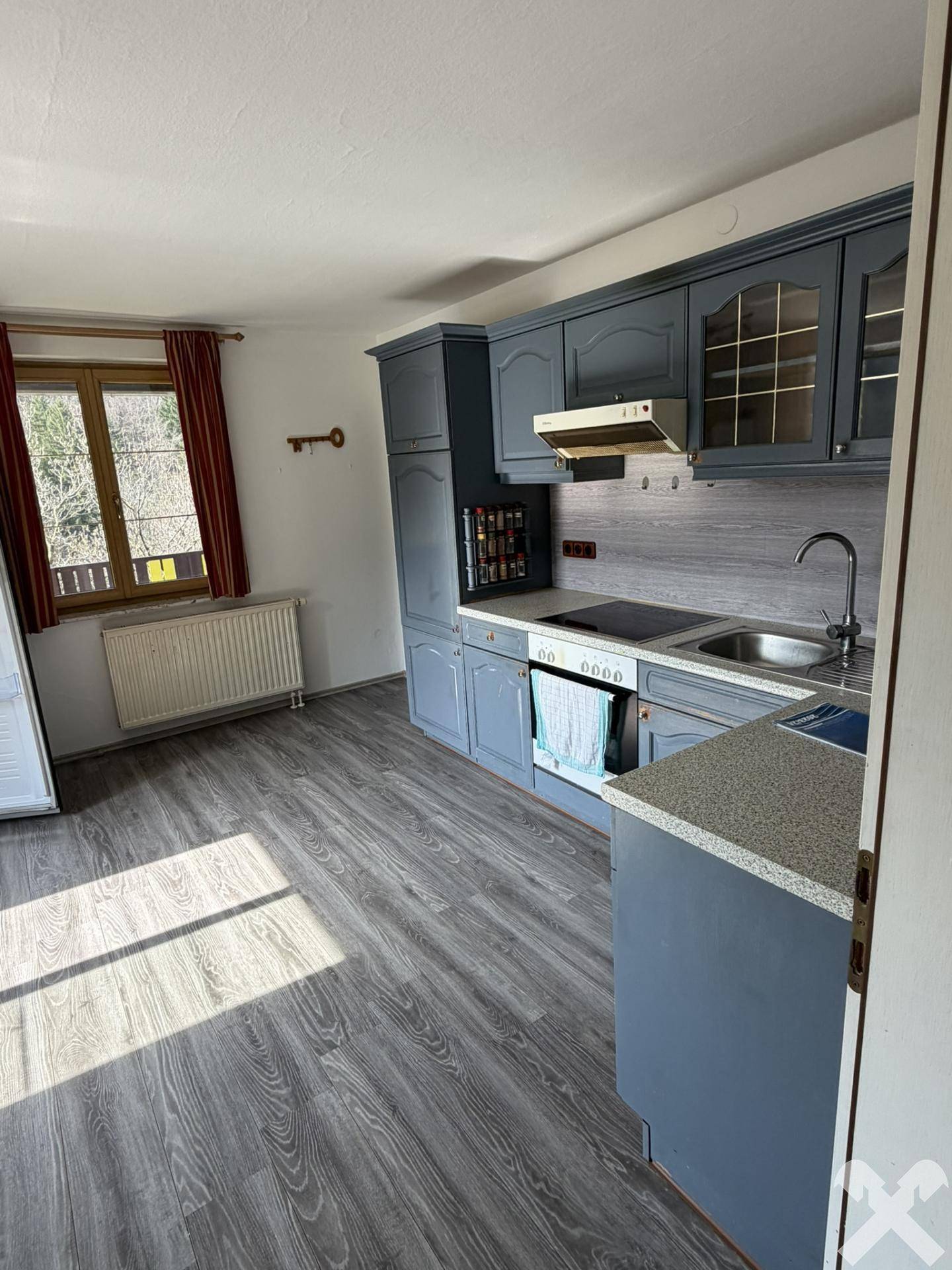 Küche mit blauen Schränken, integriertem Herd und Spüle, sowie Laminatboden.