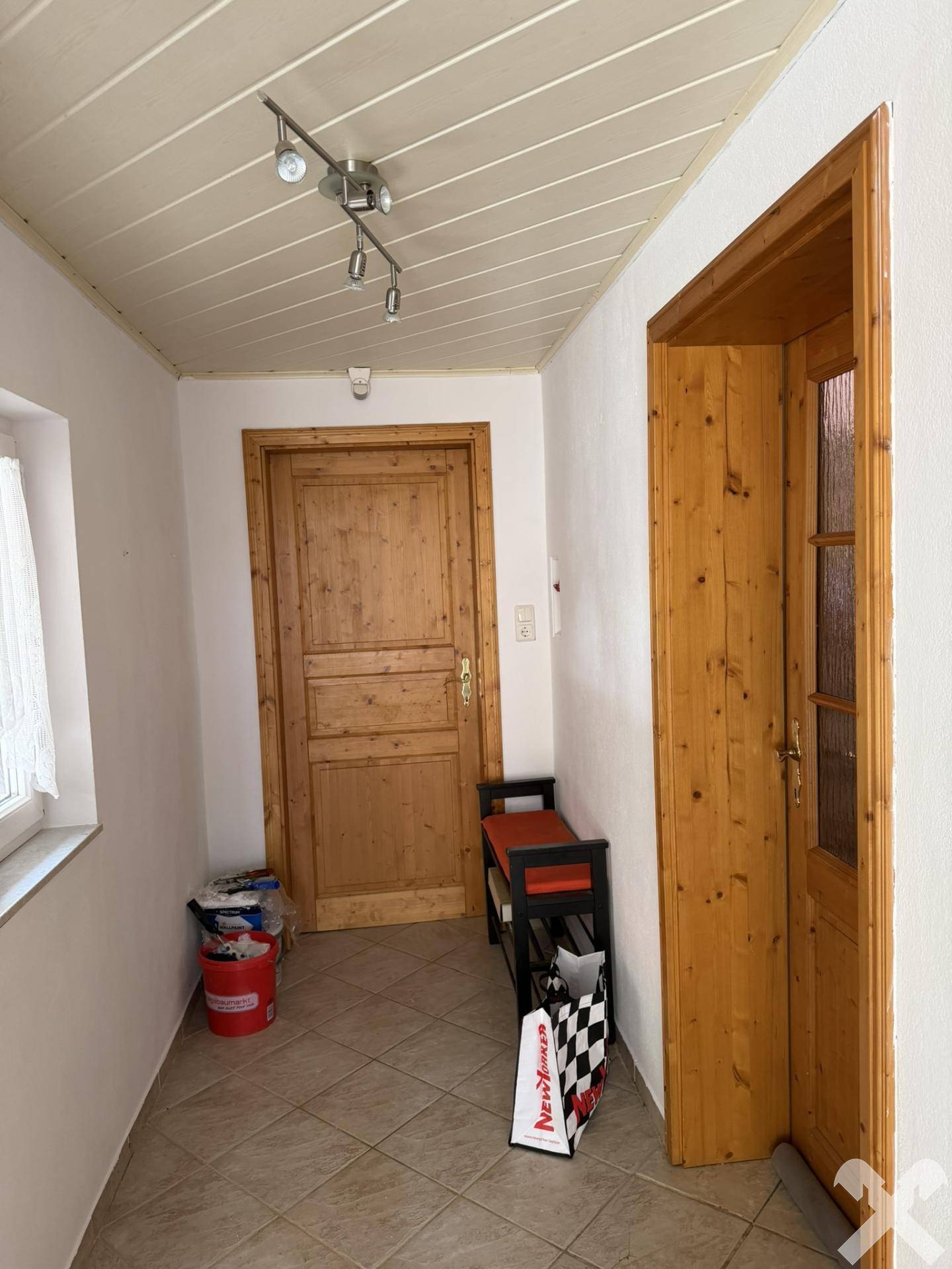 Heller Eingangsbereich mit Fliesenboden und Holztüren, der zu weiteren Räumen führt.