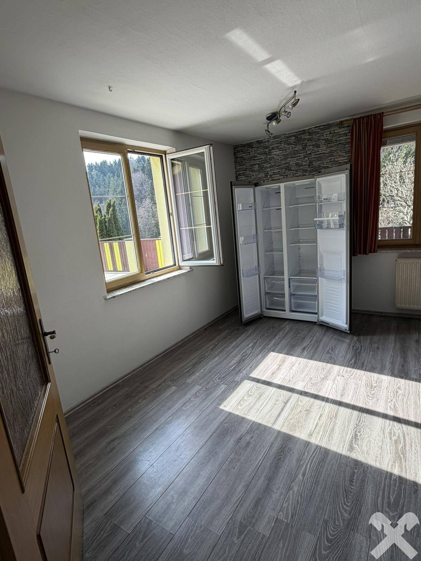 Heller Raum mit Laminatboden und großem Kühlschrank, bietet vielseitige Nutzungsmöglichkeiten.
