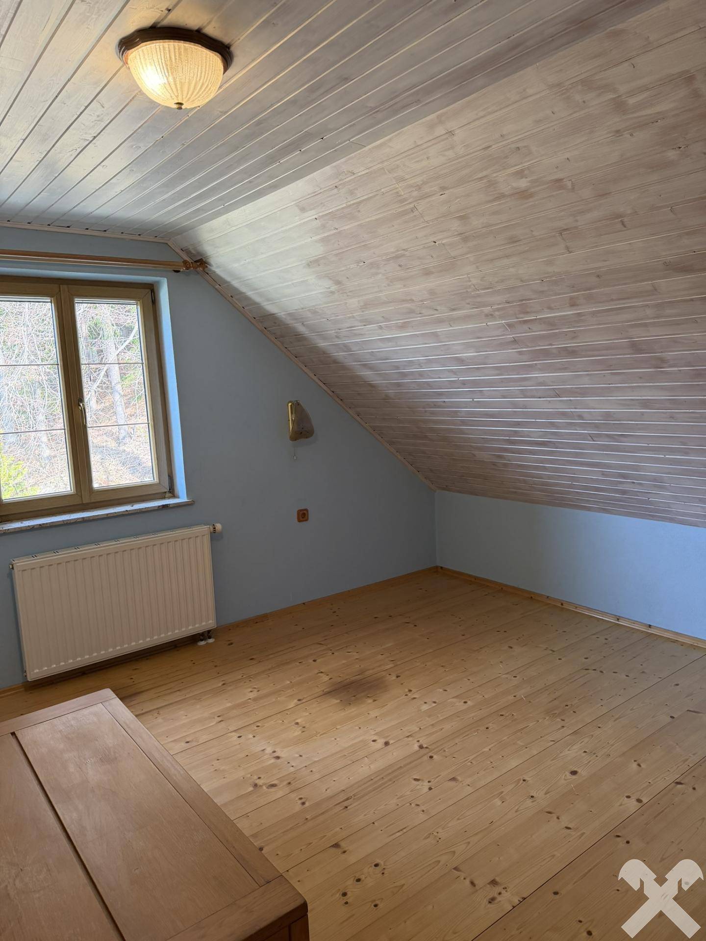 Schlafzimmer im Dachgeschoss mit Holzboden und blauen Wänden, unter einer Holzdecke.