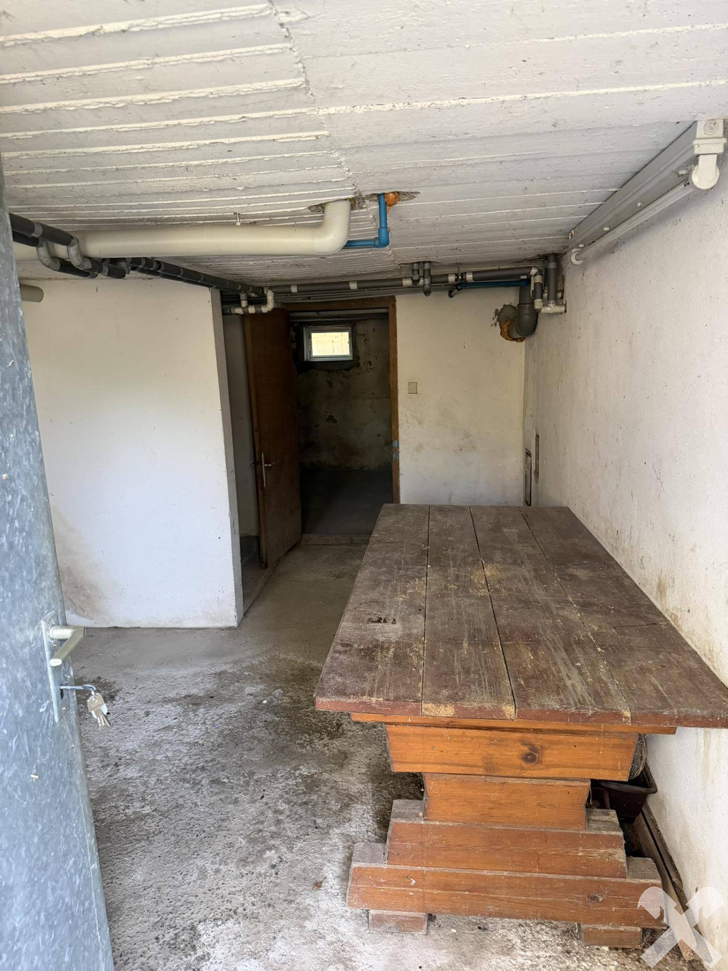 Kellerraum mit Holztisch und Betonboden, ideal als Werkstatt oder Lagerfläche.