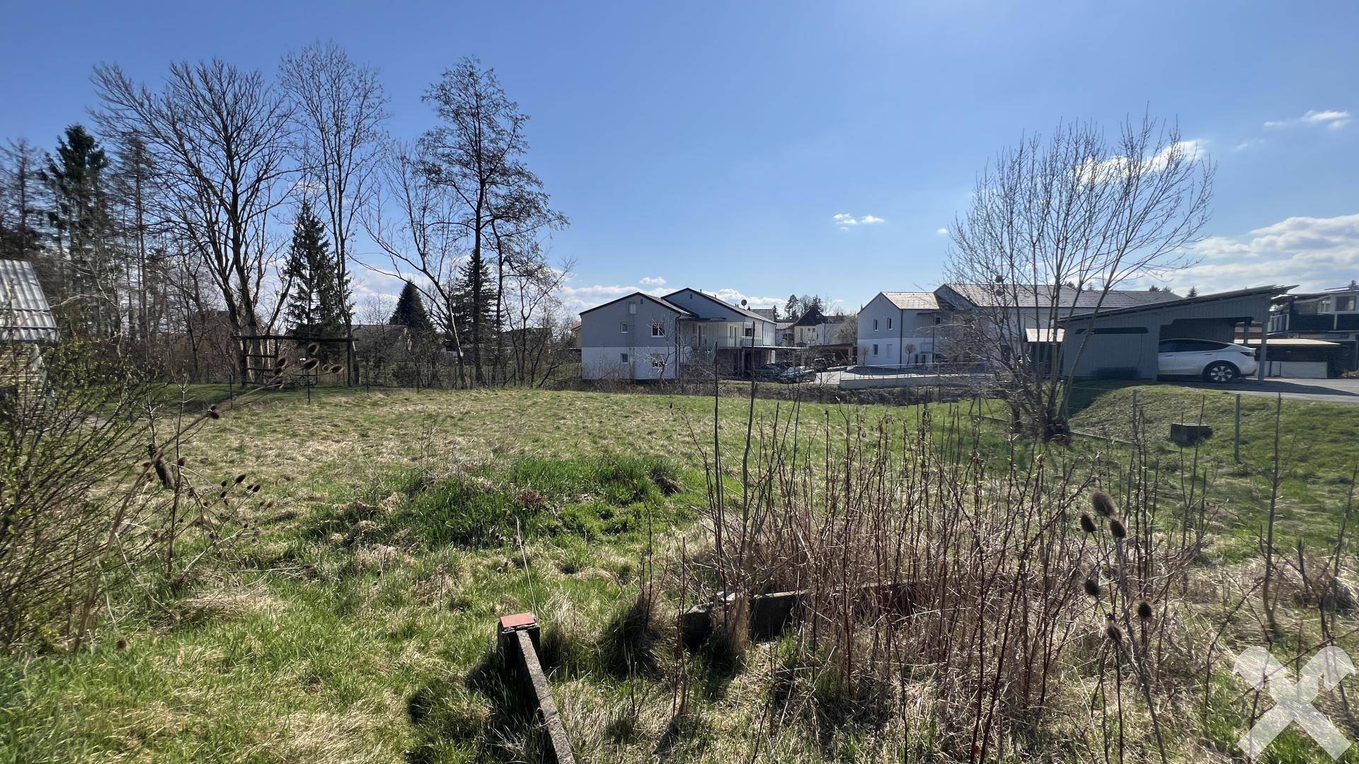 Grünes Grundstück mit hohem Gras und Blick auf moderne Wohnhäuser in der Nachbarschaft.