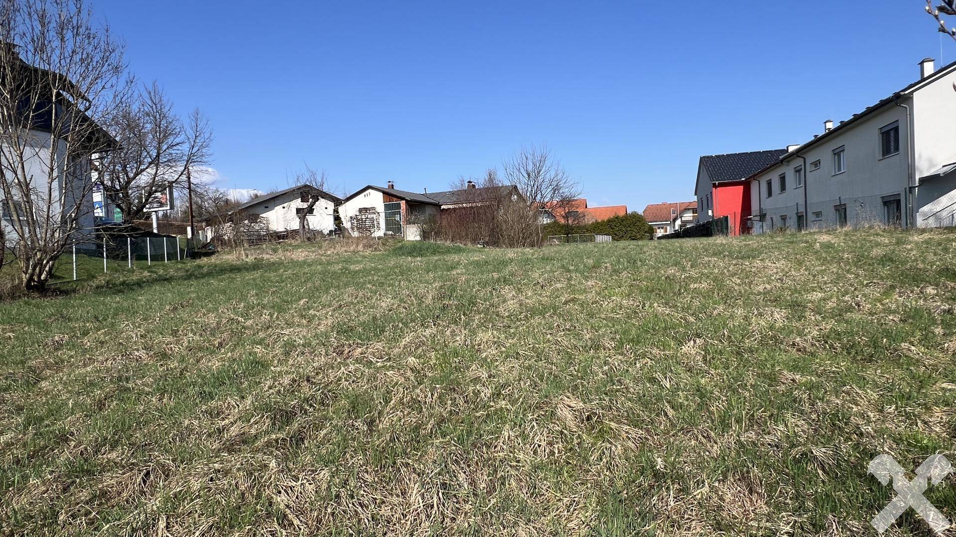 Offenes Grundstück mit Grasbewuchs und angrenzenden Wohnhäusern unter klarem Frühlingshimmel.