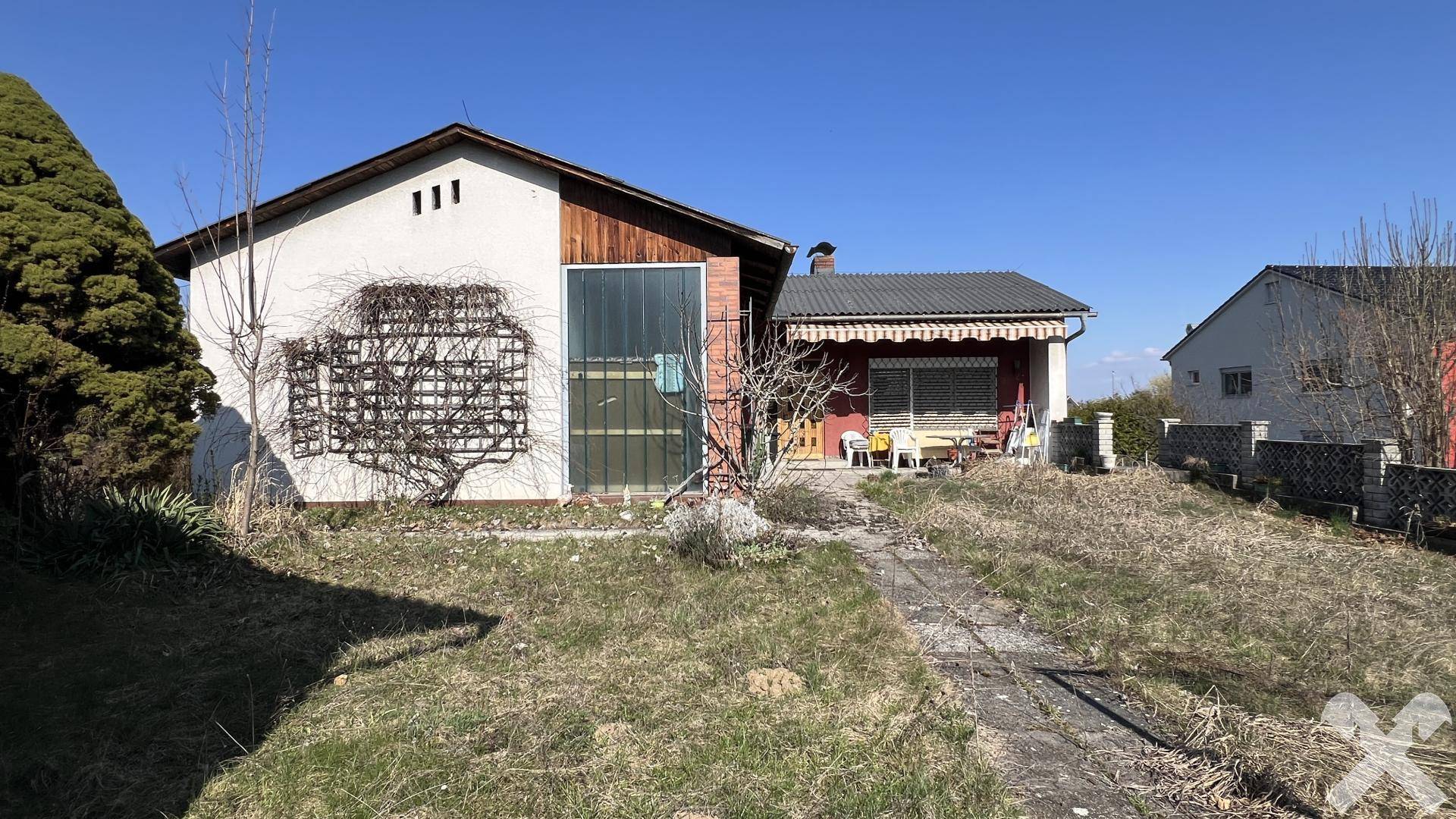 Einfamilienhaus mit überdachter Terrasse und Gartenbereich, umgeben von Bäumen und Sträuchern.