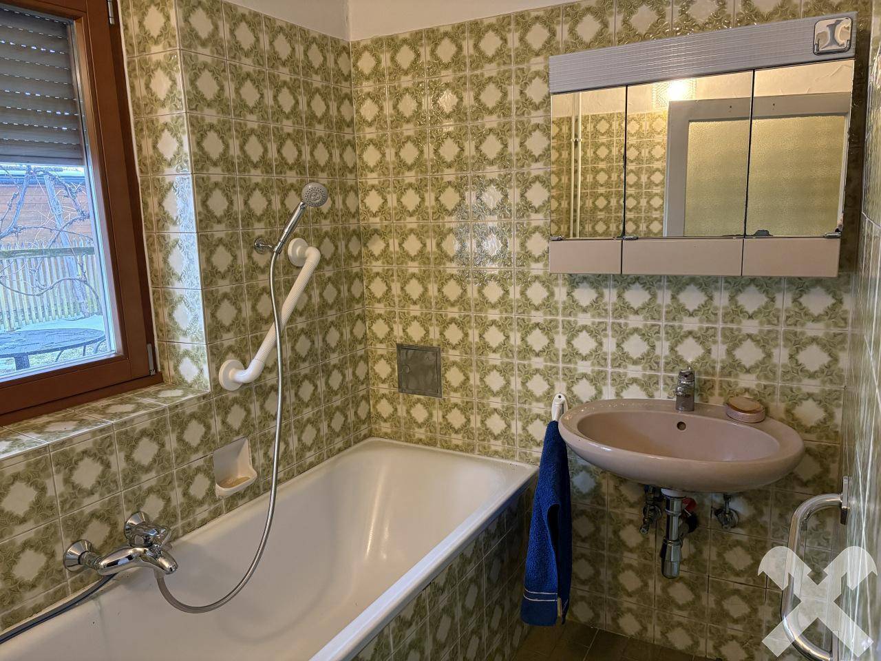 Badezimmer mit Badewanne, Waschbecken und gemusterten grünen Wandfliesen.
