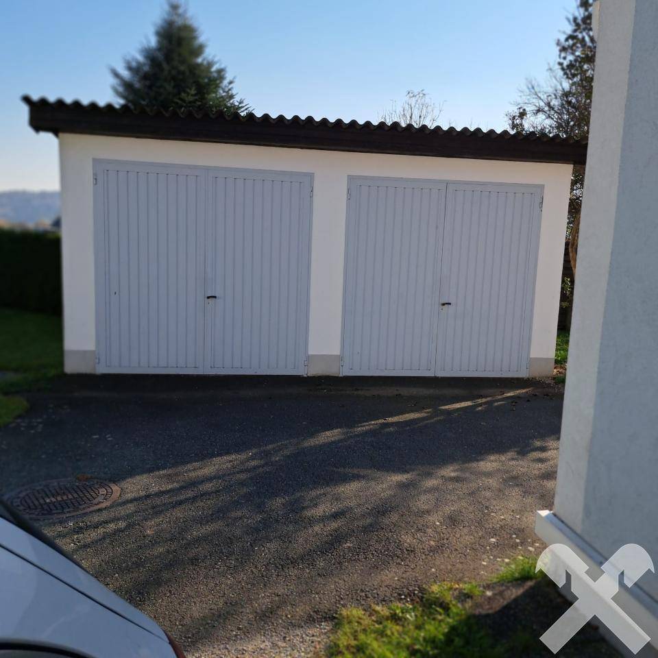 Doppelgarage mit zwei hellgrauen Toren und einem gepflasterten Vorplatz.