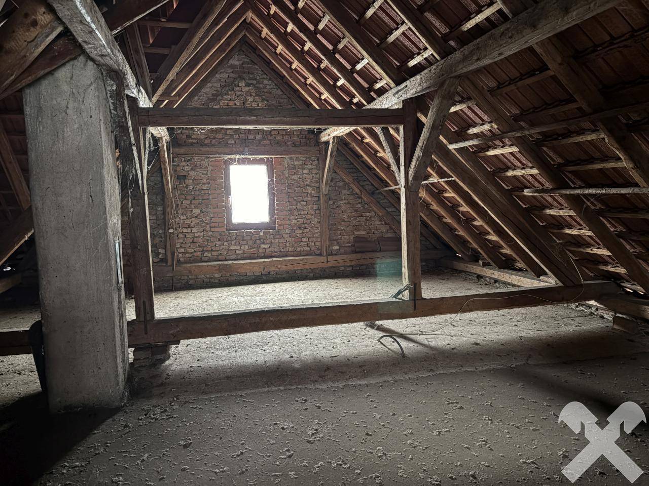Unausgebauter Dachboden mit sichtbaren Holzbalken und einem kleinen Fenster.