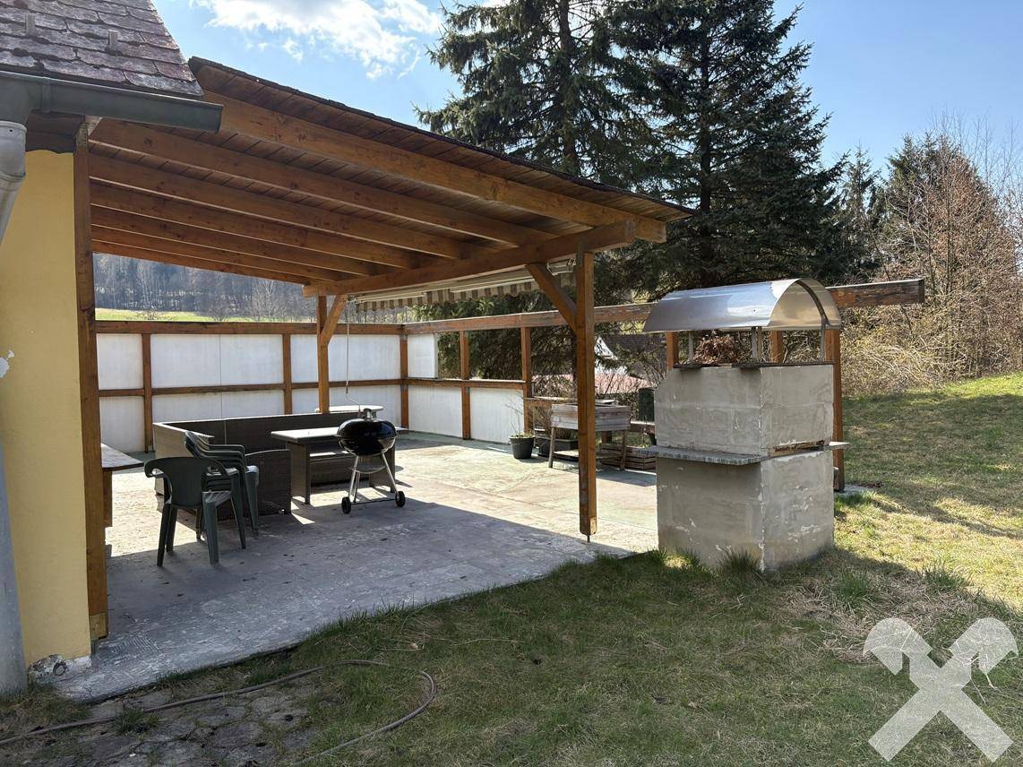 Überdachte Terrasse mit Grillplatz und Sitzgelegenheiten, ideal für gesellige Stunden im Freien.