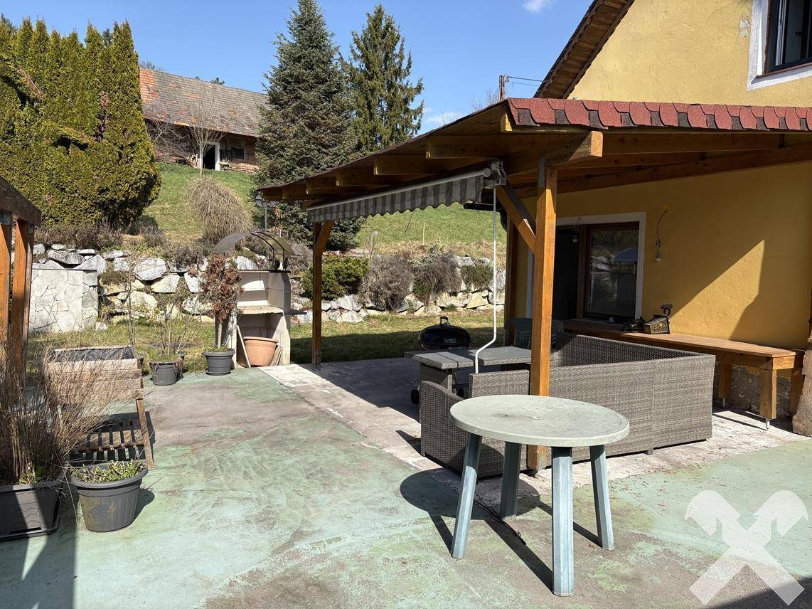 Gemütlicher überdachter Terrassenbereich mit verschiedenen Sitzmöglichkeiten und Blick ins Grüne.
