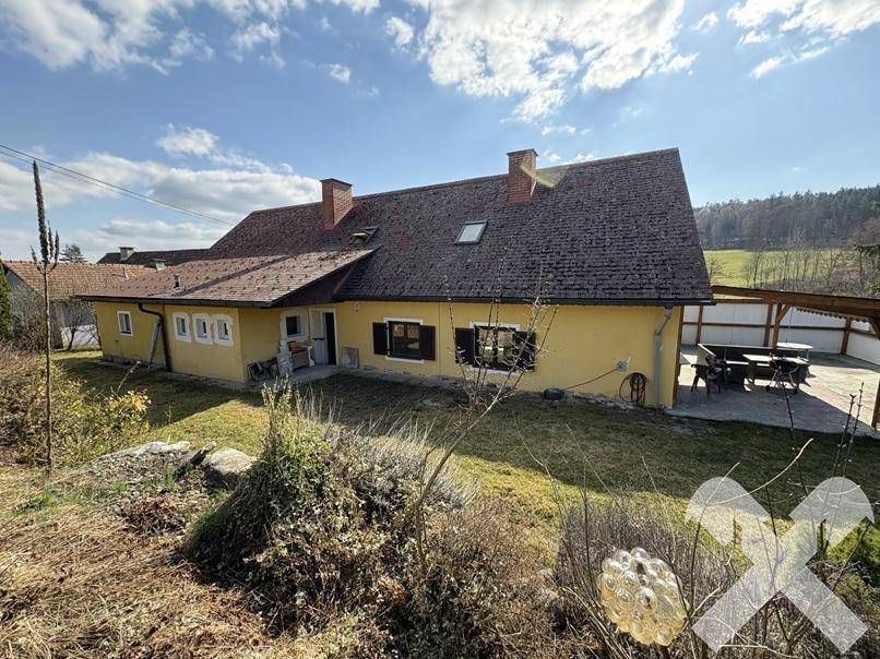 Rückansicht des Hauses mit Garten, Rasenfläche und überdachtem Sitzbereich im Freien.