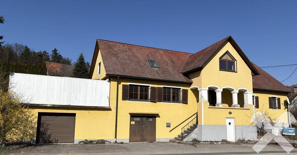 Ansicht des gelben Wohnhauses mit Anbau und braunem Garagentor unter blauem Himmel.