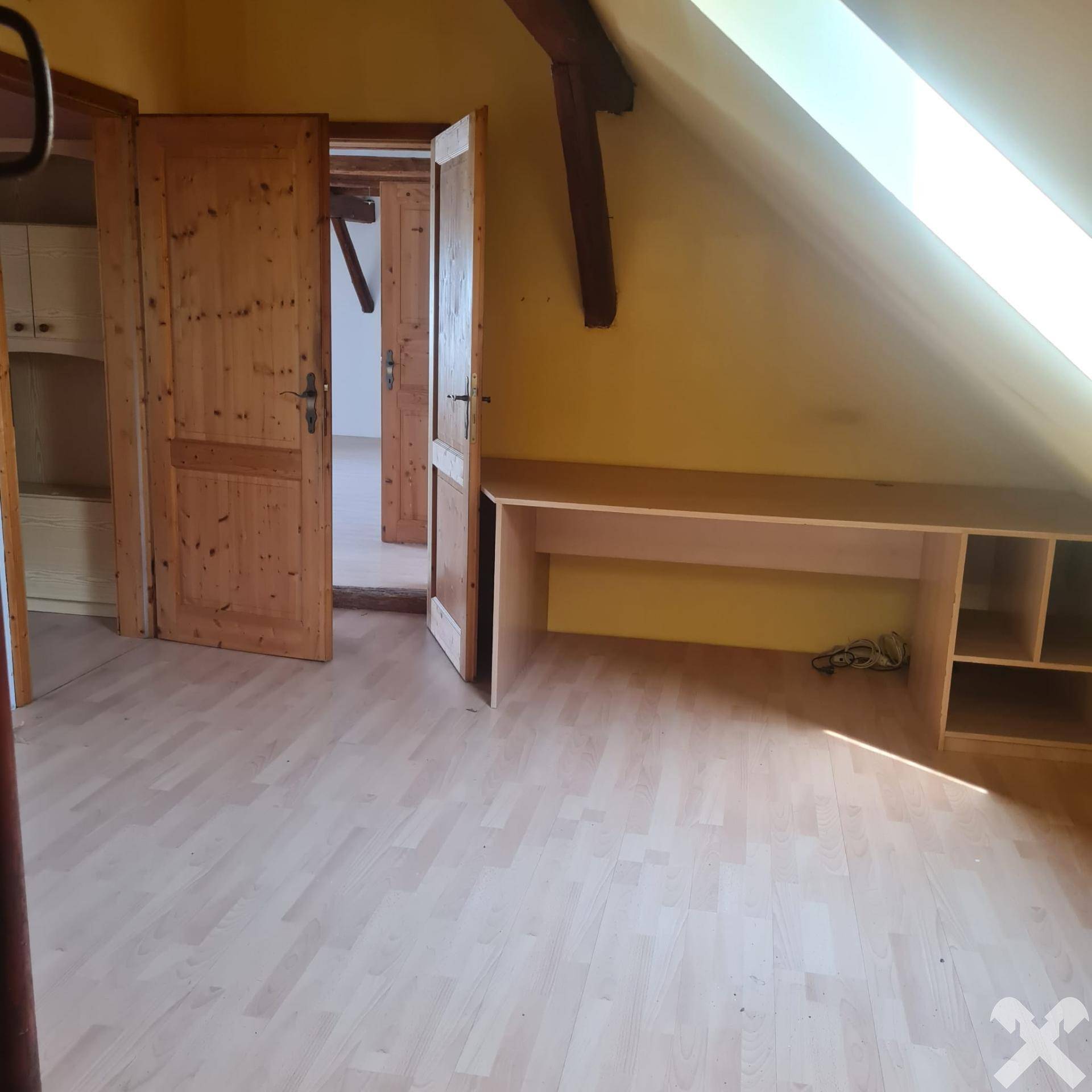 Dachgeschossraum mit Holztüren, Laminatboden und einem eingebauten Schreibtisch unter der Schräge.