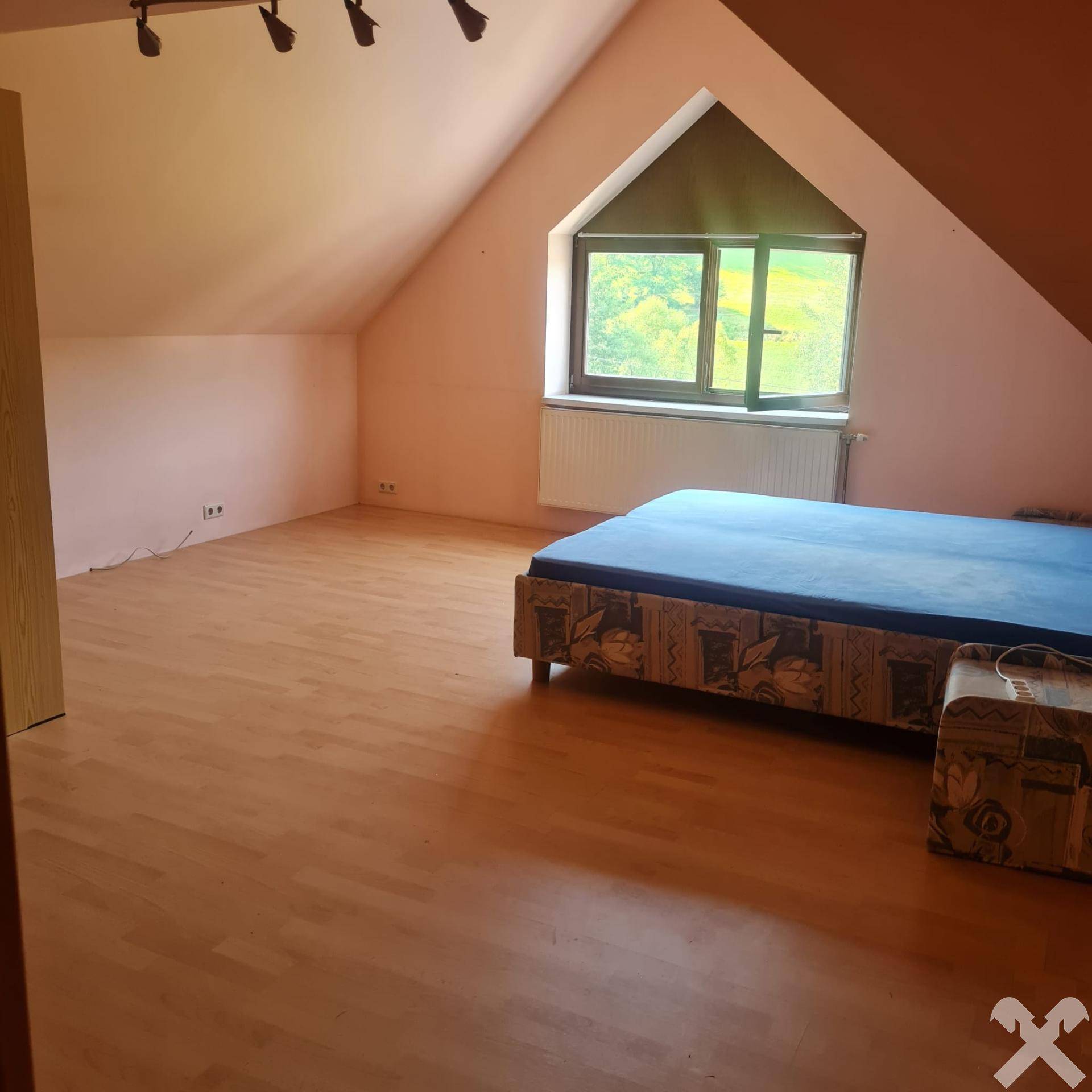 Schlafzimmer im Dachgeschoss mit schrägen Wänden, Laminatboden und Blick ins Grüne.
