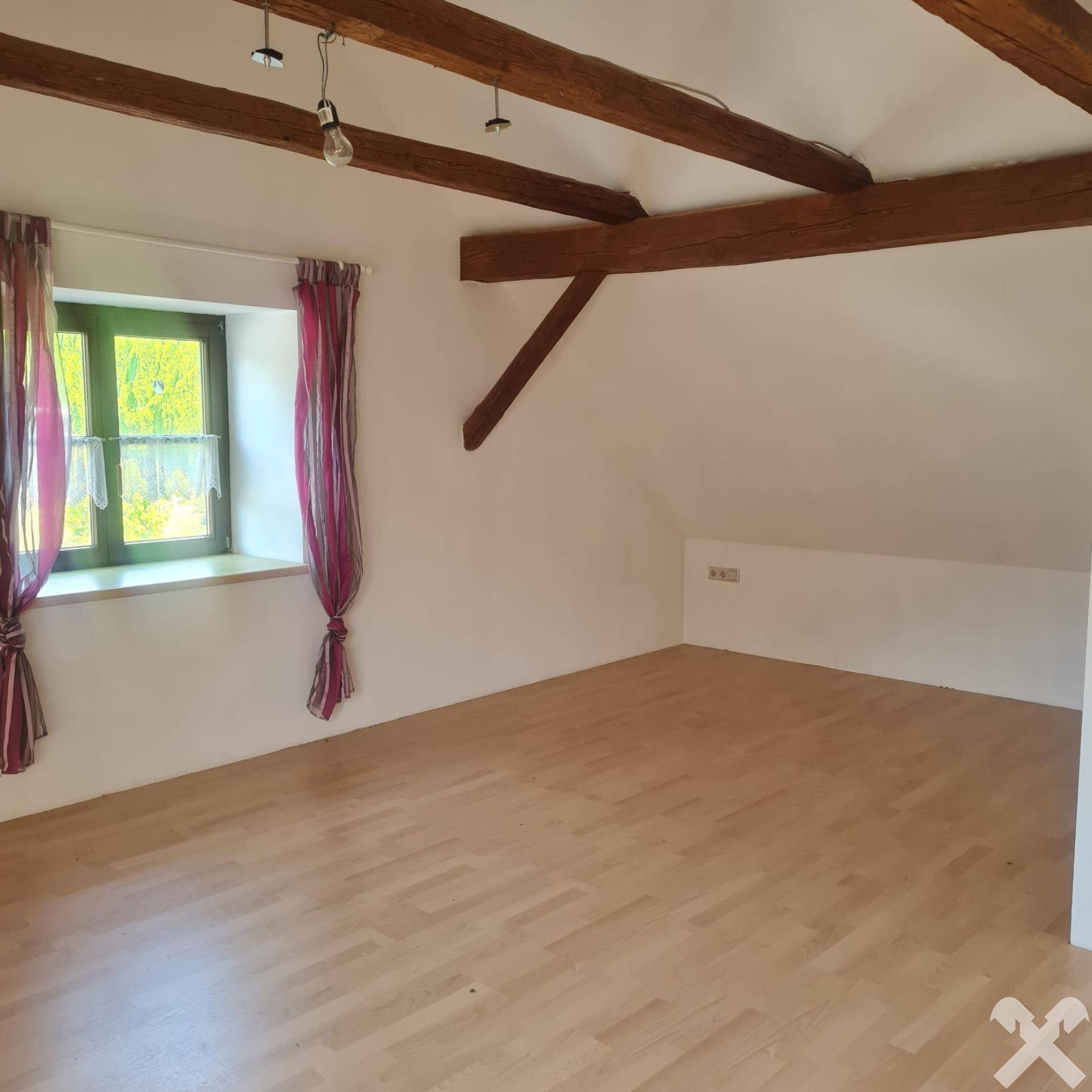 Heller Raum mit Holzbalken an der Decke und Laminatboden, bereit zur individuellen Gestaltung.