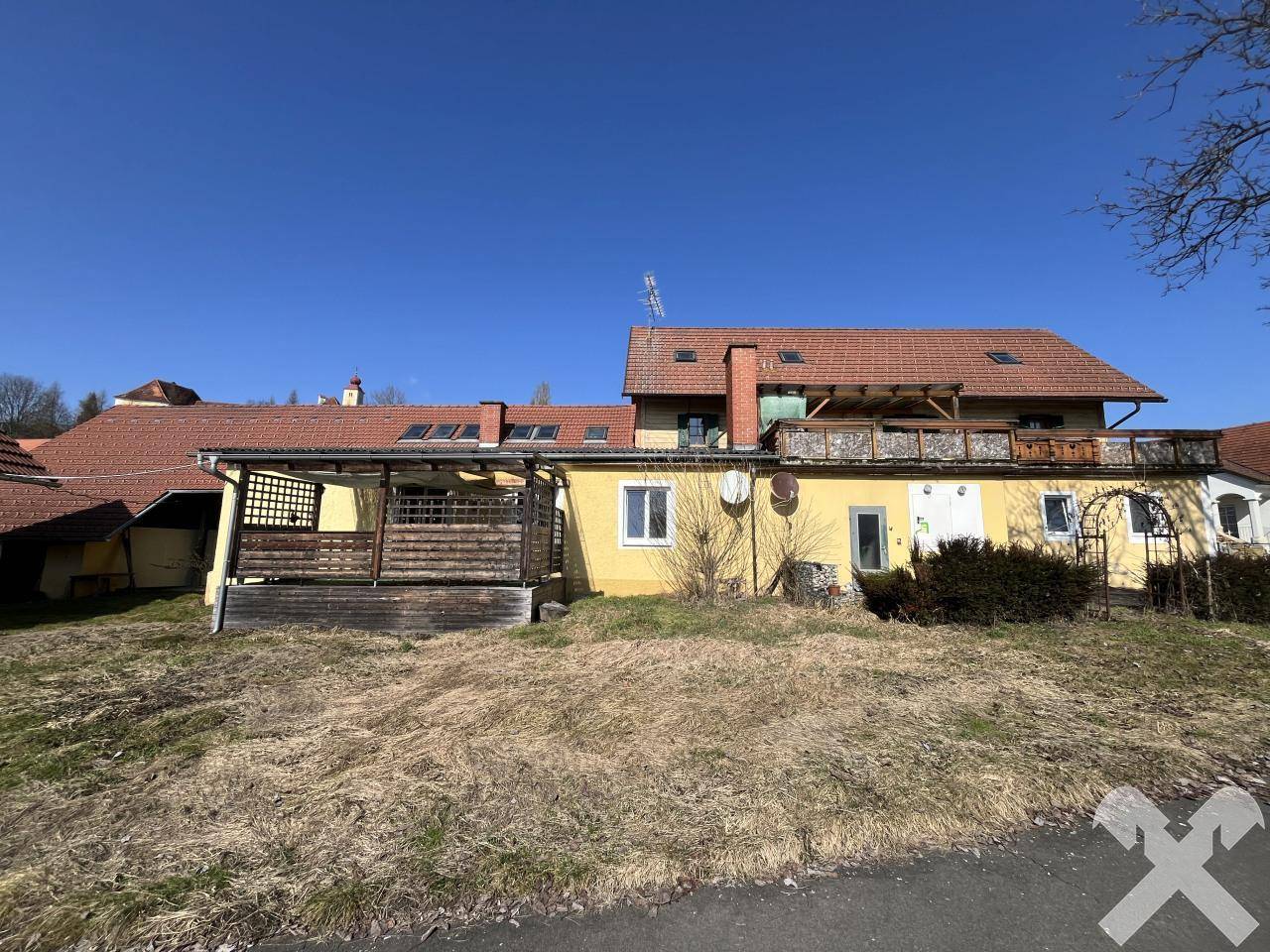 Rückansicht des Gebäudes mit einer überdachten Terrasse und einem weitläufigen Gartenbereich.