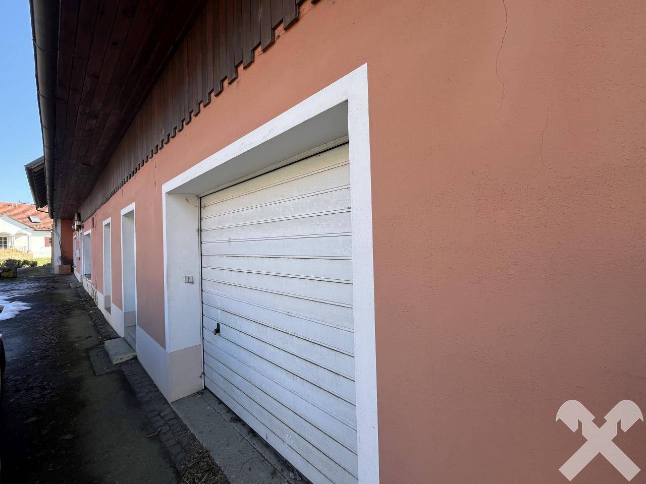 Nahaufnahme eines Garagentors an einem Gebäude mit rötlicher Fassade und weißem Rahmen.