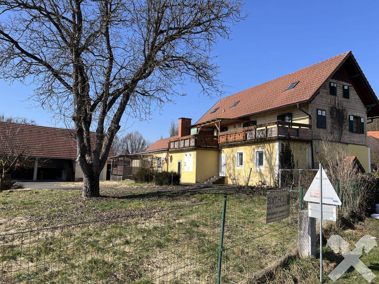 Weitläufige Außenansicht des Anwesens mit großem Baum, Gartenbereich und dem Hauptgebäude im Hintergrund.