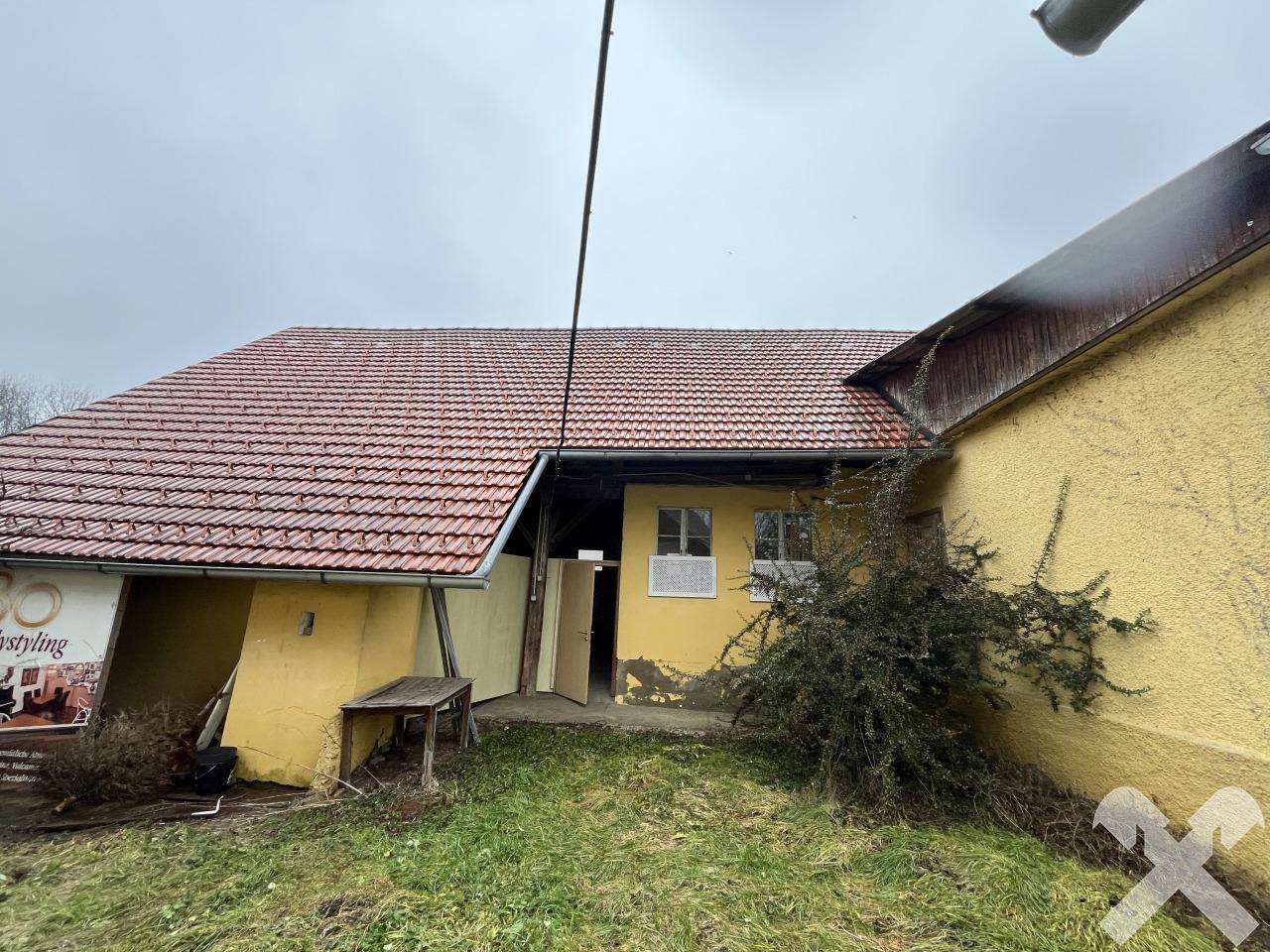 Seitenansicht eines Nebengebäudes mit Ziegeldach und gelber Fassade, umgeben von Grünflächen.