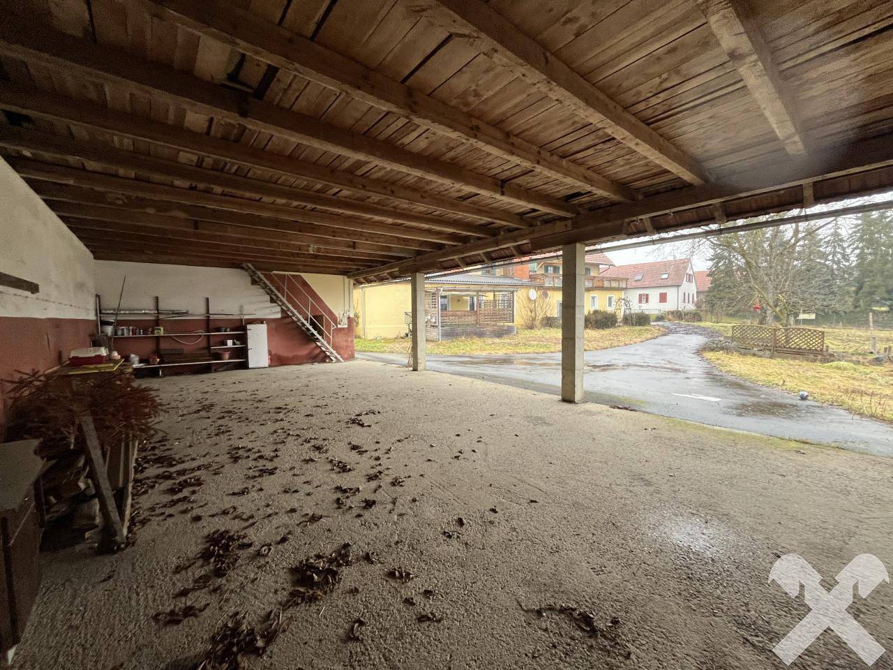 Geräumiger Innenraum einer Garage oder Lagerhalle mit Holzbalkendecke und Schotterboden.