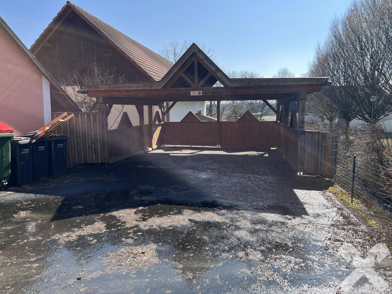 Rustikaler Holzcarport mit Satteldach und angrenzendem Zaun, bietet geschützten Parkraum.