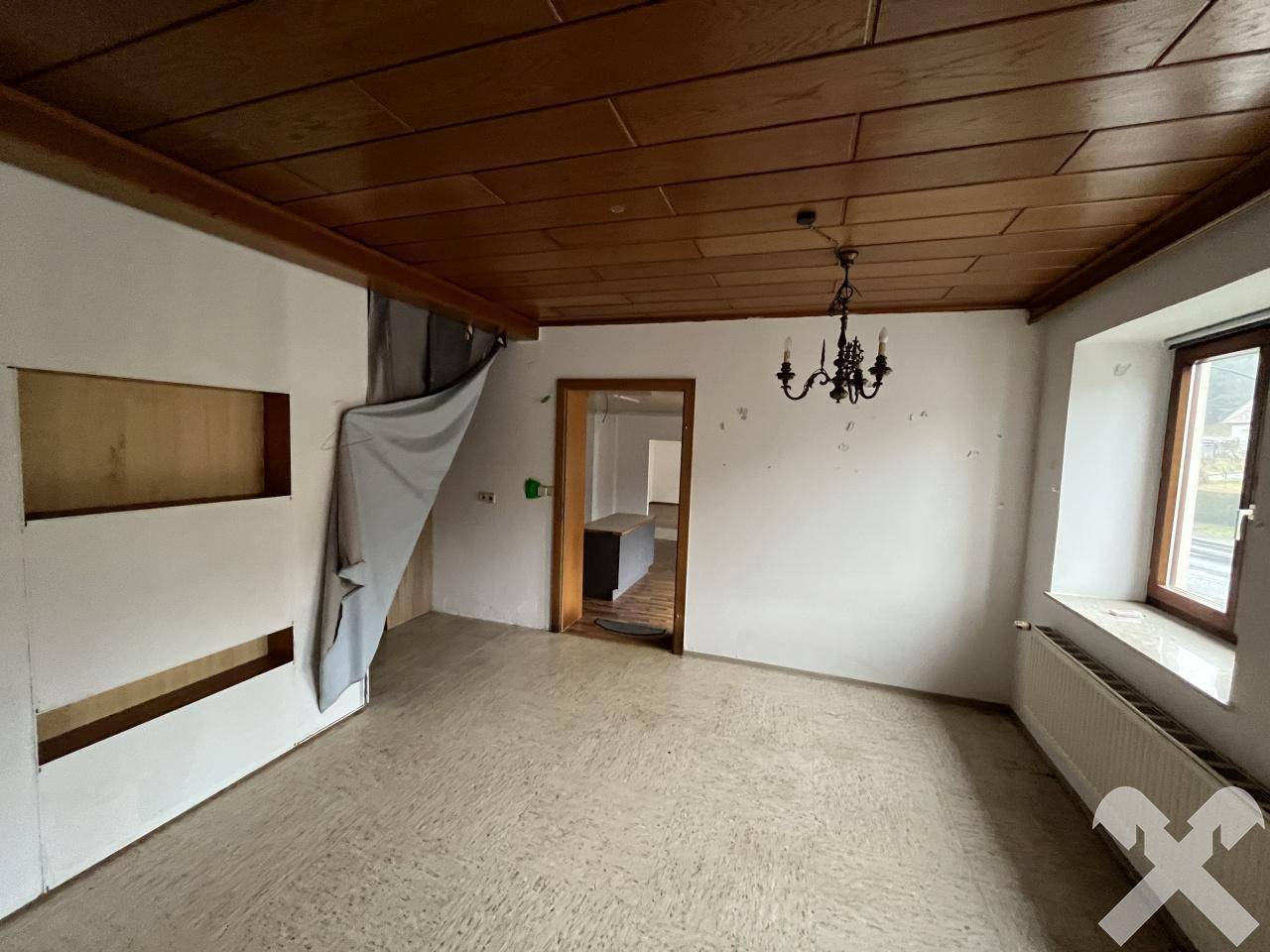 Raum mit Holztäfelung an der Decke, weiß gestrichenen Wänden und einem Kronleuchter.