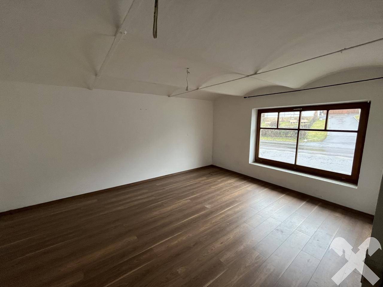 Leerer Raum mit Holzboden und einem großen Fenster, das viel Tageslicht hereinlässt.
