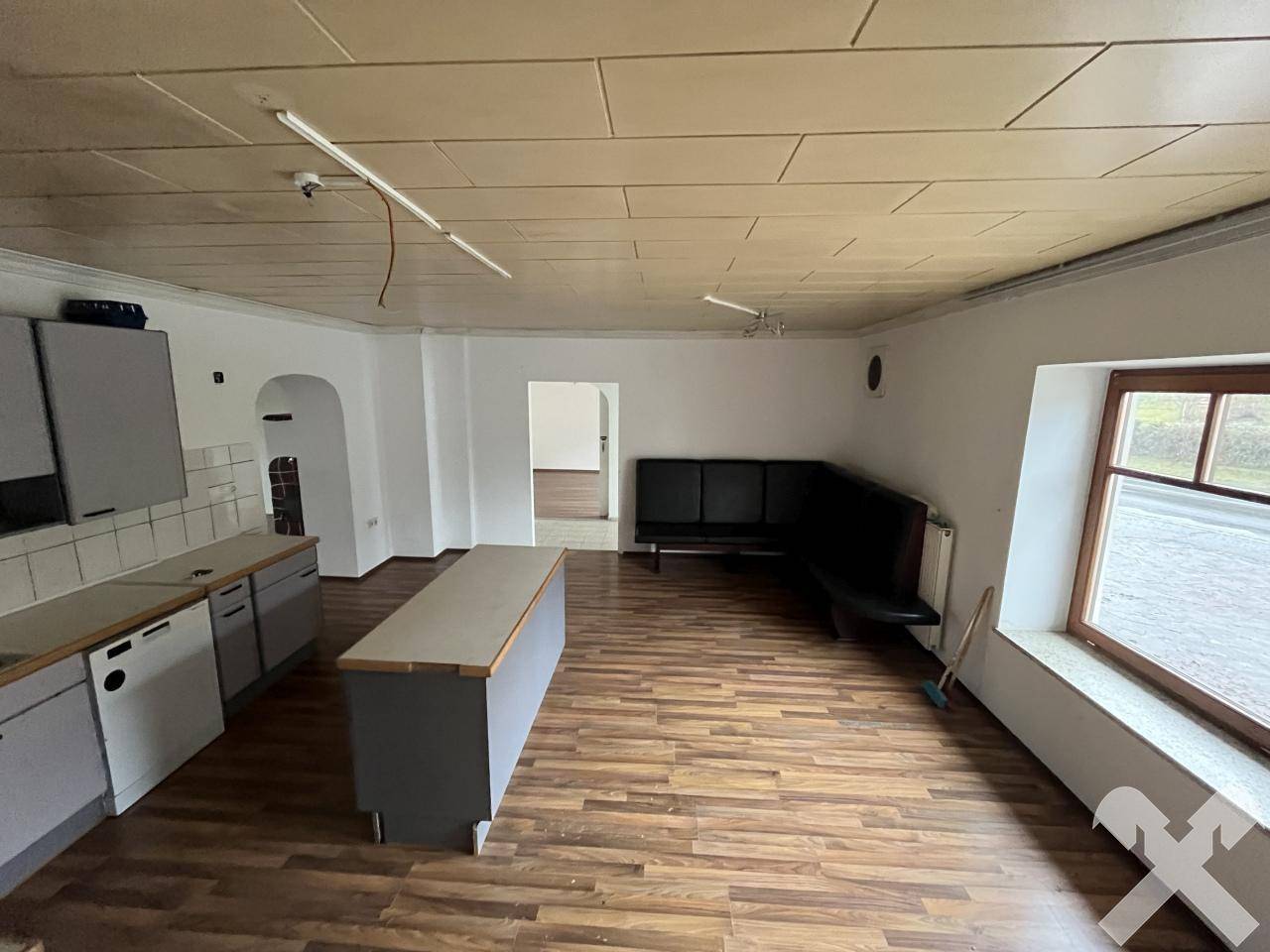 Offener Wohnbereich mit Küchenzeile, Holzboden und Sitzbank am Fenster.