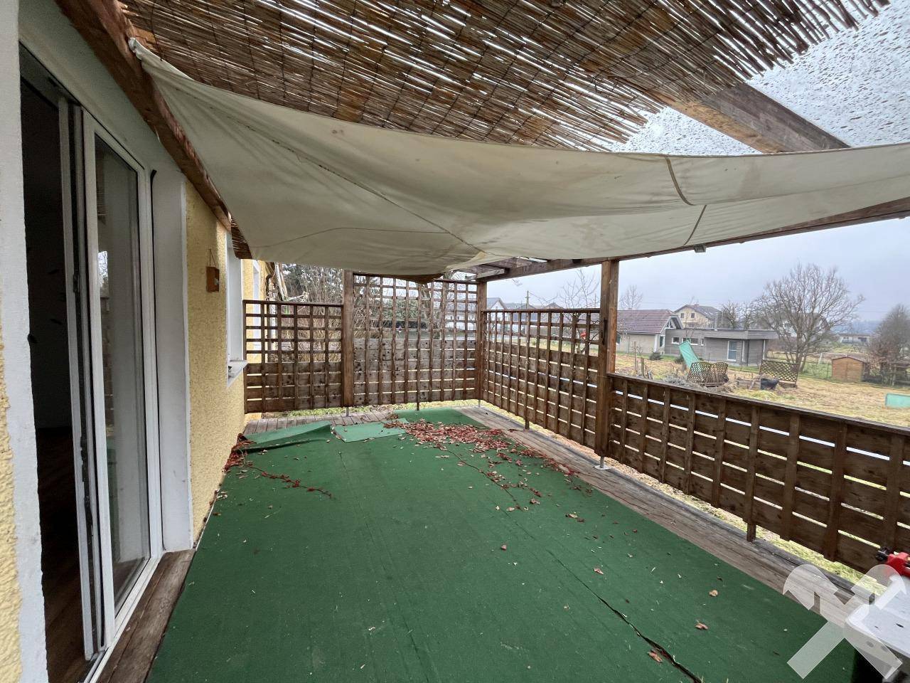 Überdachte Terrasse mit Holzboden und Gitterzaun, ideal für entspannte Stunden im Freien.