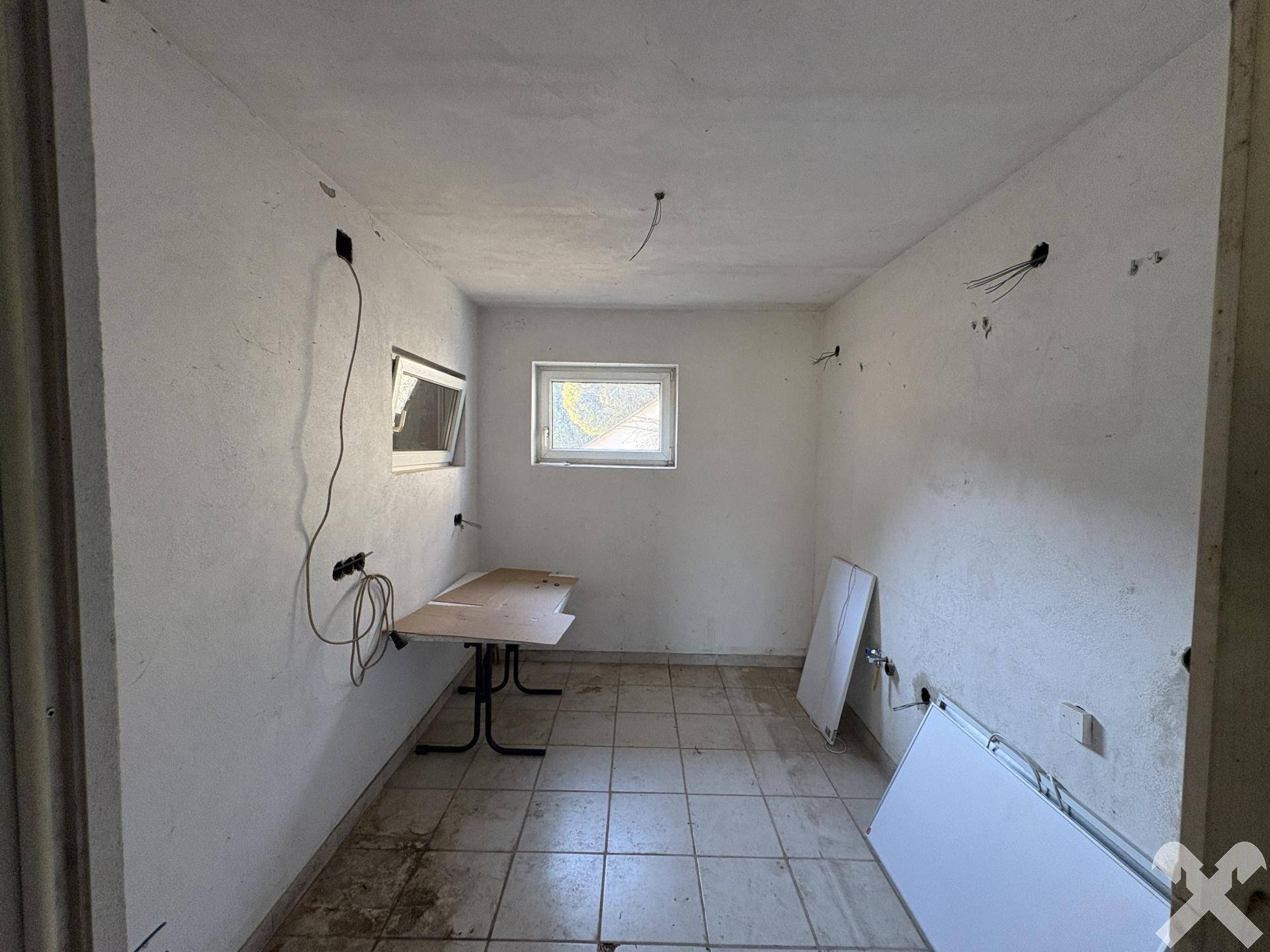 Einfacher Raum mit Fliesenboden und Verkabelung, bereit für den Ausbau.