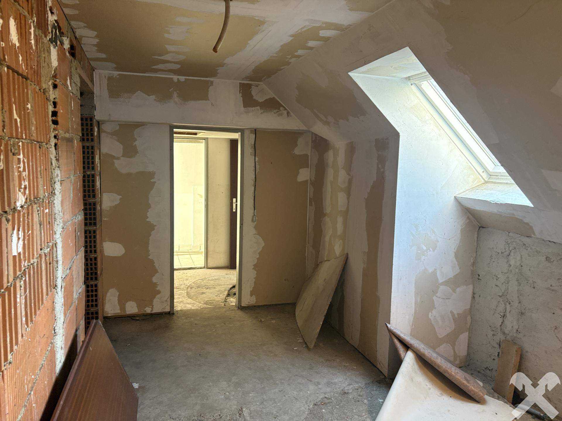 Dachgeschossraum im Rohbau mit Dachschräge und Dachfenster.