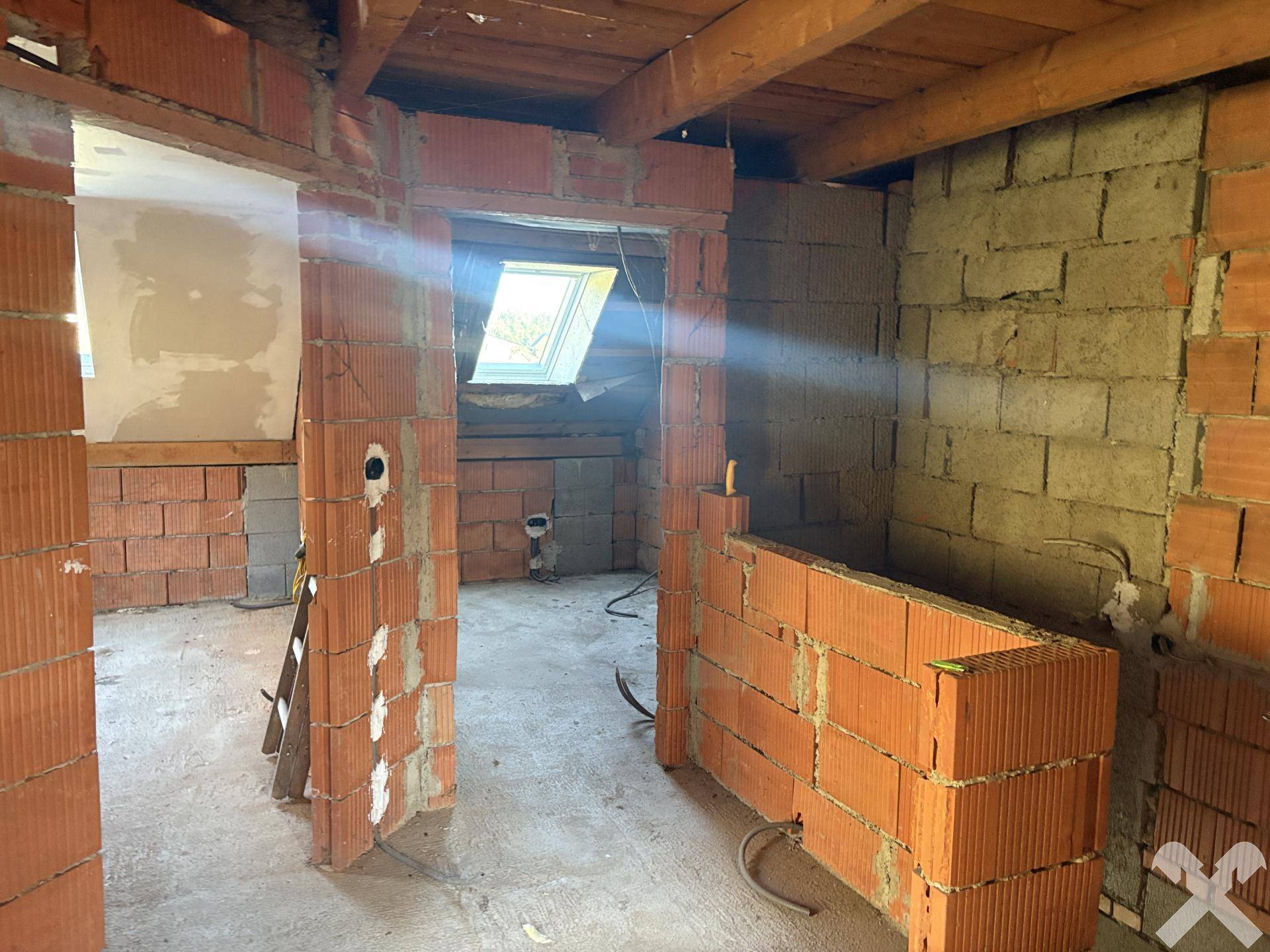 Dachgeschoss im Rohbau mit Ziegelwänden und sichtbaren Holzbalken.