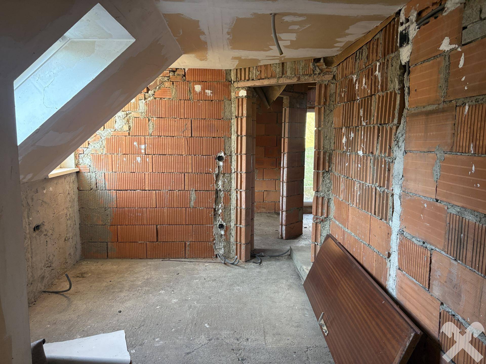 Dachgeschoss im Rohbau mit Ziegelwänden und Dachfenster.