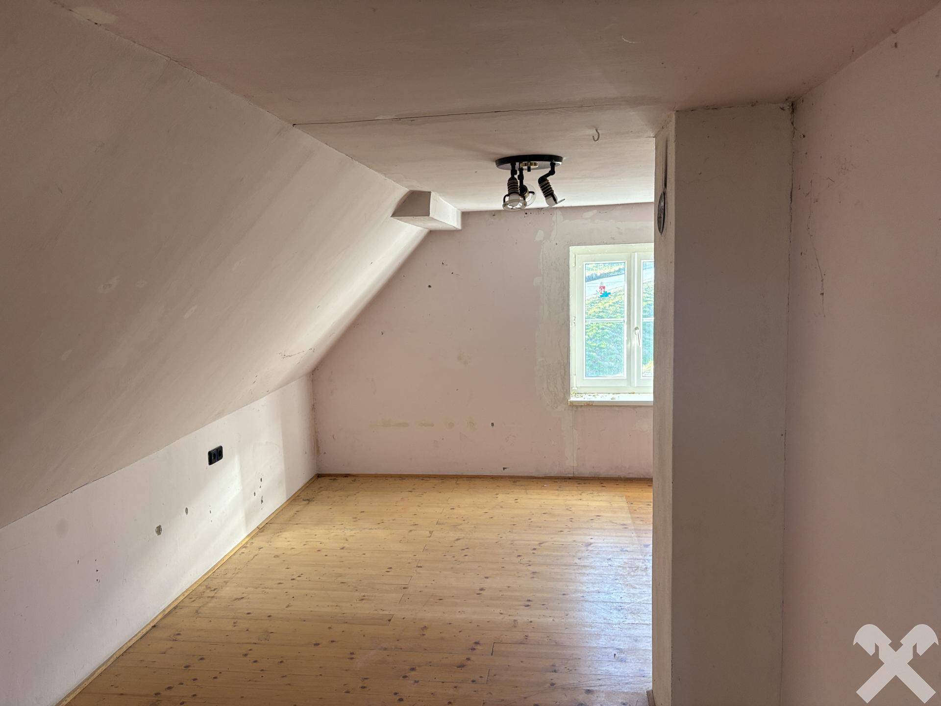 Fertiger Dachgeschossraum mit Holzfußboden, Dachschräge und Fenster.