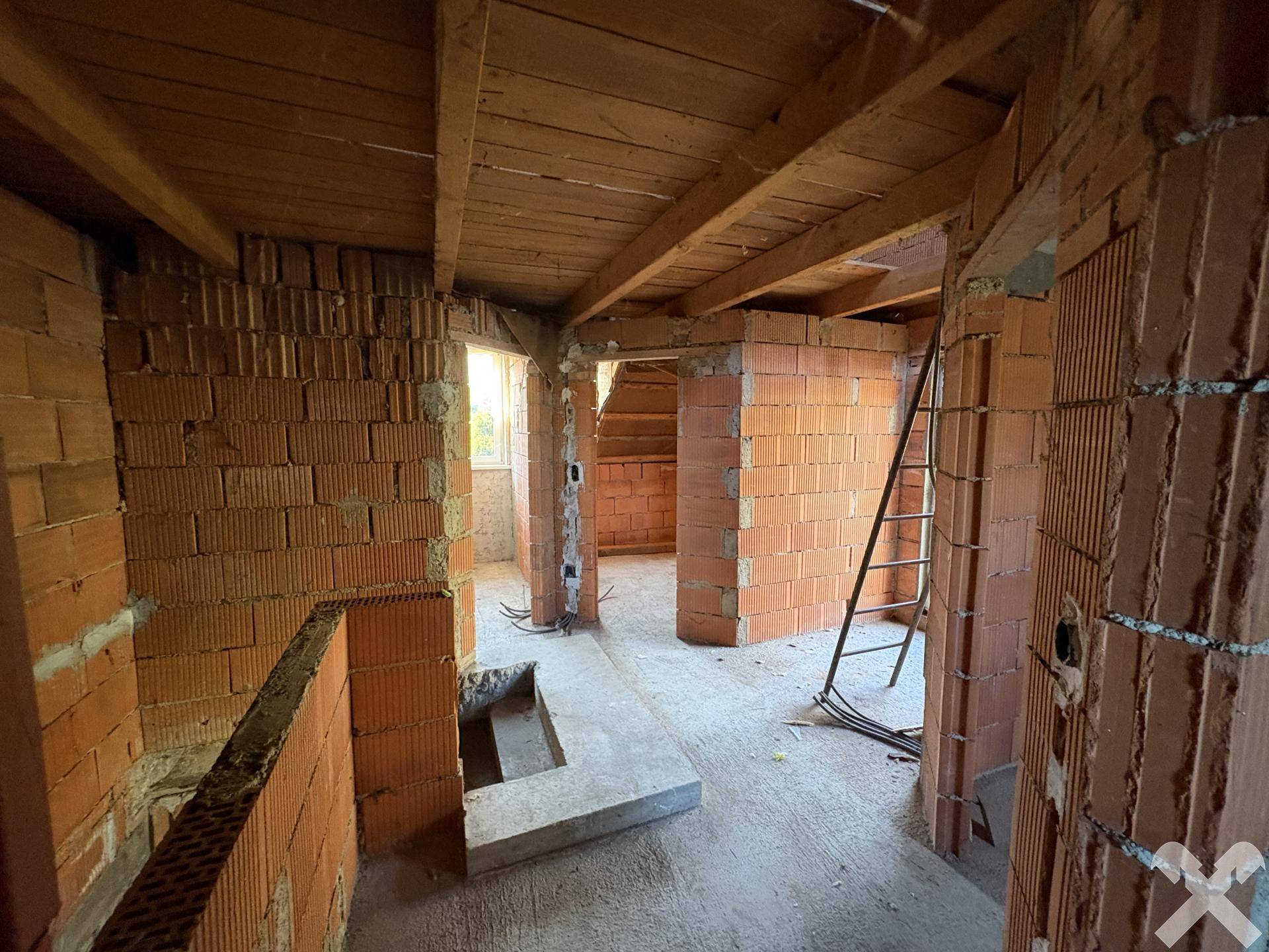 Dachgeschoss im Rohbau mit Ziegelwänden, Holzbalken und Treppenaufgang.